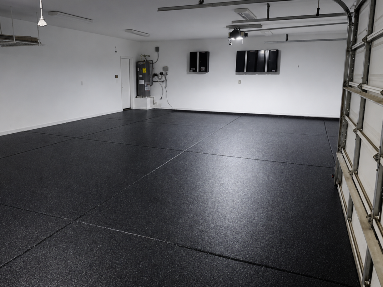 Empty garage with black rubber flooring, white walls, and storage cabinets on the wall.