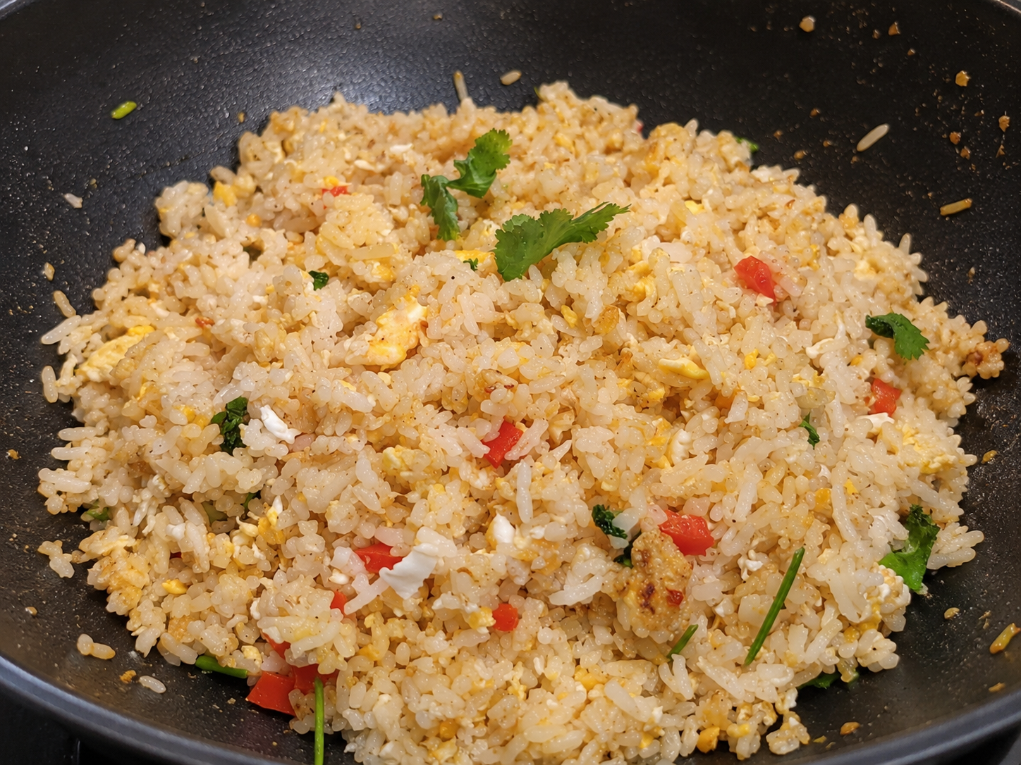 Close-up of fried rice with scrambled eggs, chopped tomatoes, chopped greens, and cilantro garnishes in a black pan.