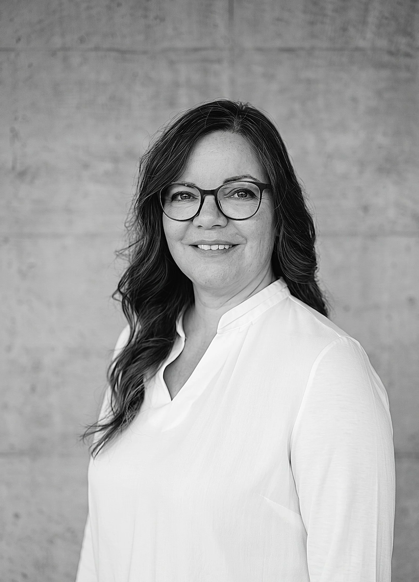 Schwarz-Weiss-Porträt von Nicole Bischof, Leiterin Administration der Innovaplus integrale Planung GmbH, im weissen Hemd vor einer Sichtbetonwand.
