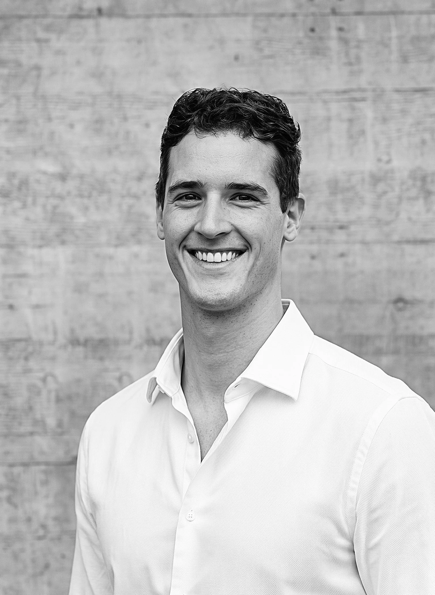 Schwarz-Weiss-Porträt von Robin Scherbl, Projektleiter Technik der Innovaplus integrale Planung GmbH, im weissen Hemd vor einer Sichtbetonwand.