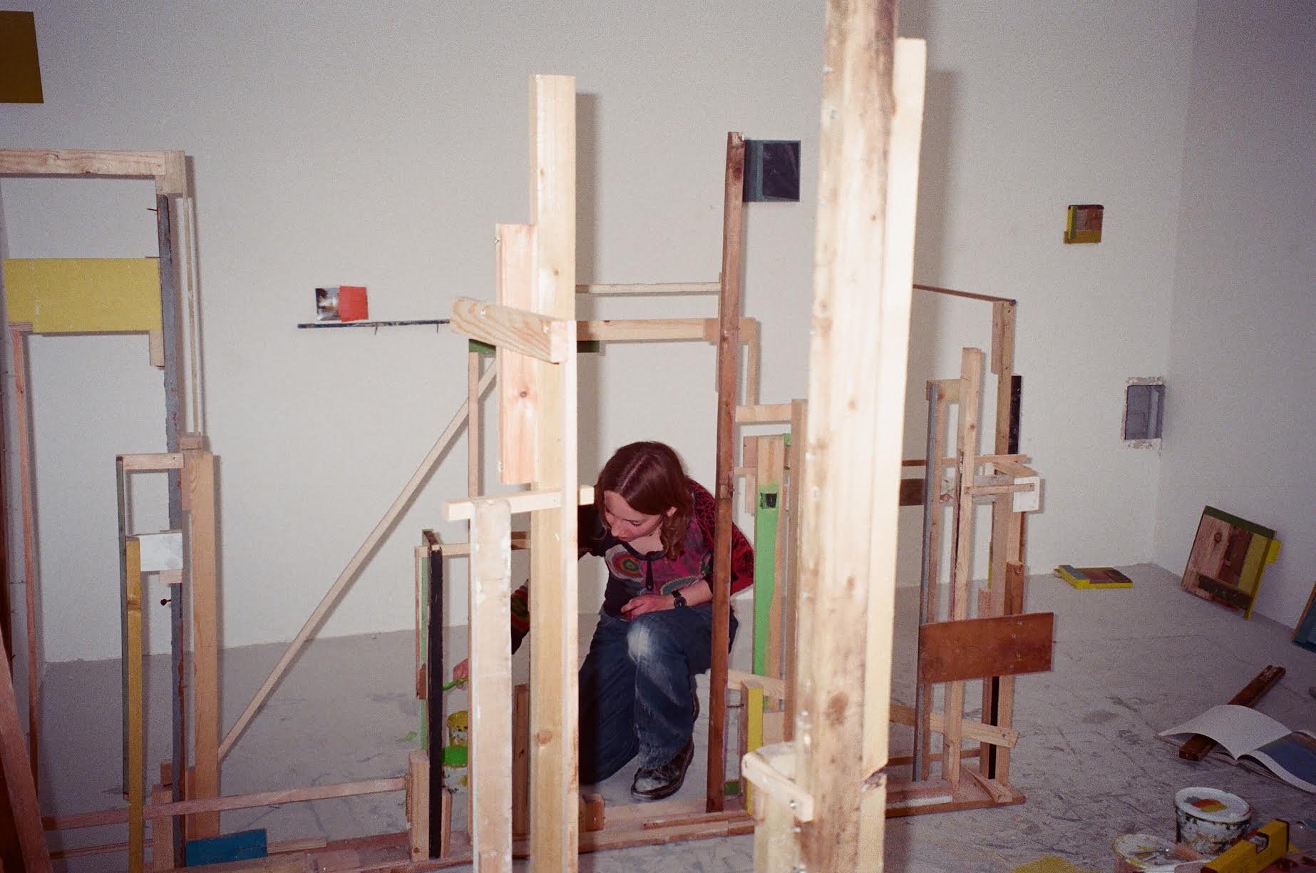A woman working on a wooden structure in a room under construction, surrounded by various pieces of wood and tools.