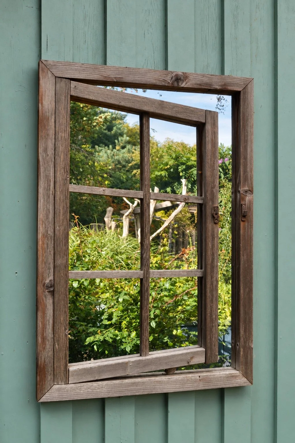 Weathered wooden mirror frame on teal-green cladding, reflecting the leafy Moray Art Centre garden.