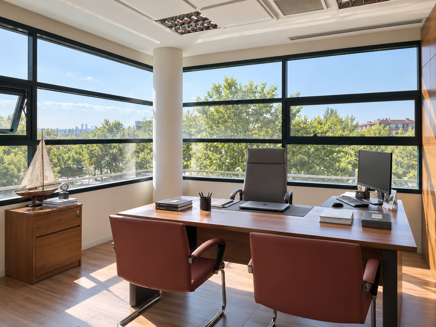 Oficina moderna con vistas a árboles y cielo despejado a través de grandes ventanas de cristal. Mueble de madera con modelo de barco y reloj en la esquina, escritorio de madera con dos sillones, una computadora, libros y artículos de oficina.