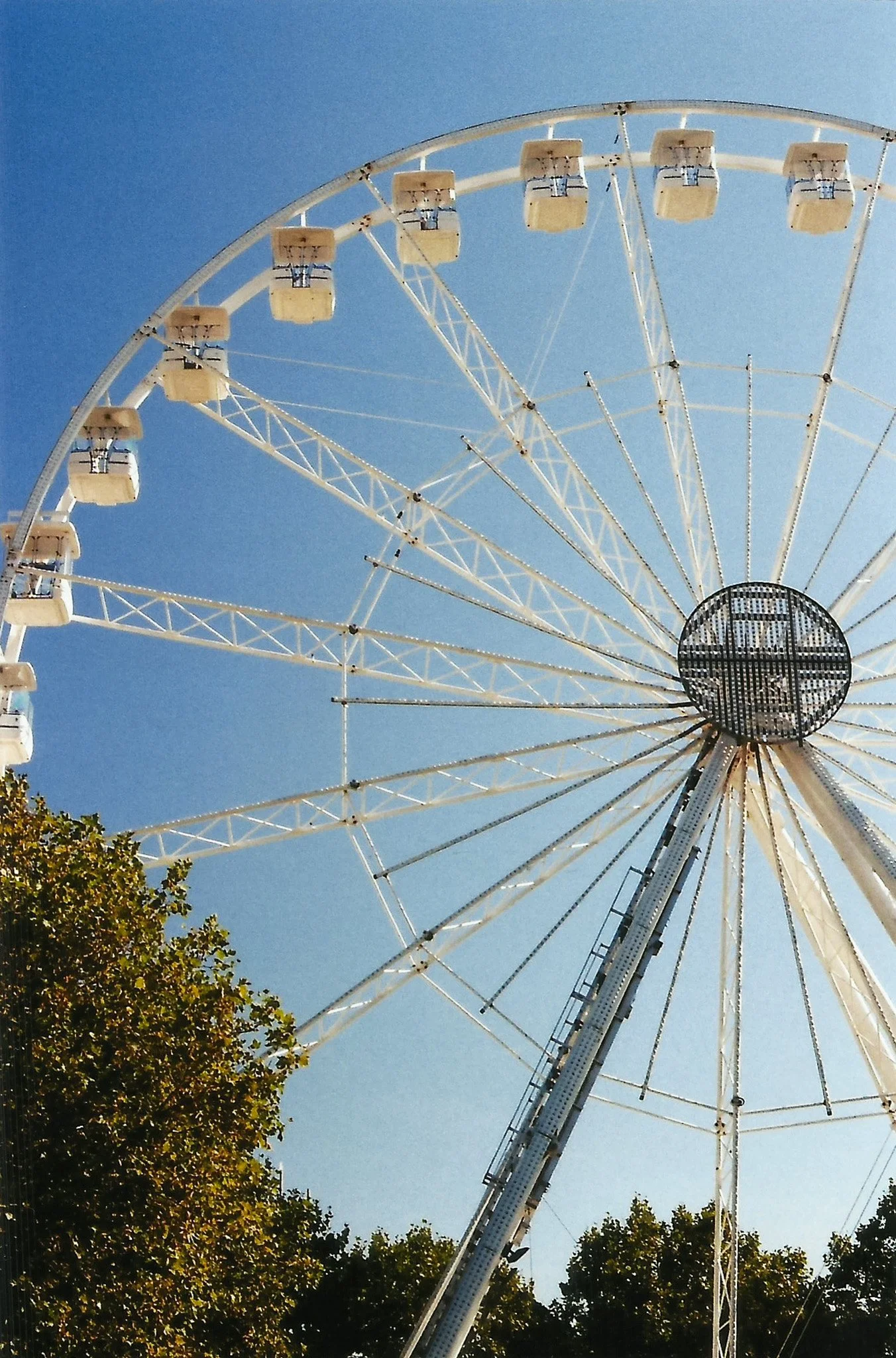 Grande roue de fête foraine avec un ciel bleu clair et des arbres au premier plan.
