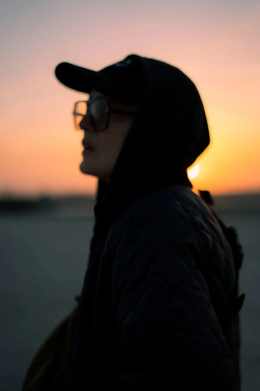 Silhouette d'une personne portant un chapeau et des lunettes, vue de profil, lors d'un coucher de soleil sur la plage.