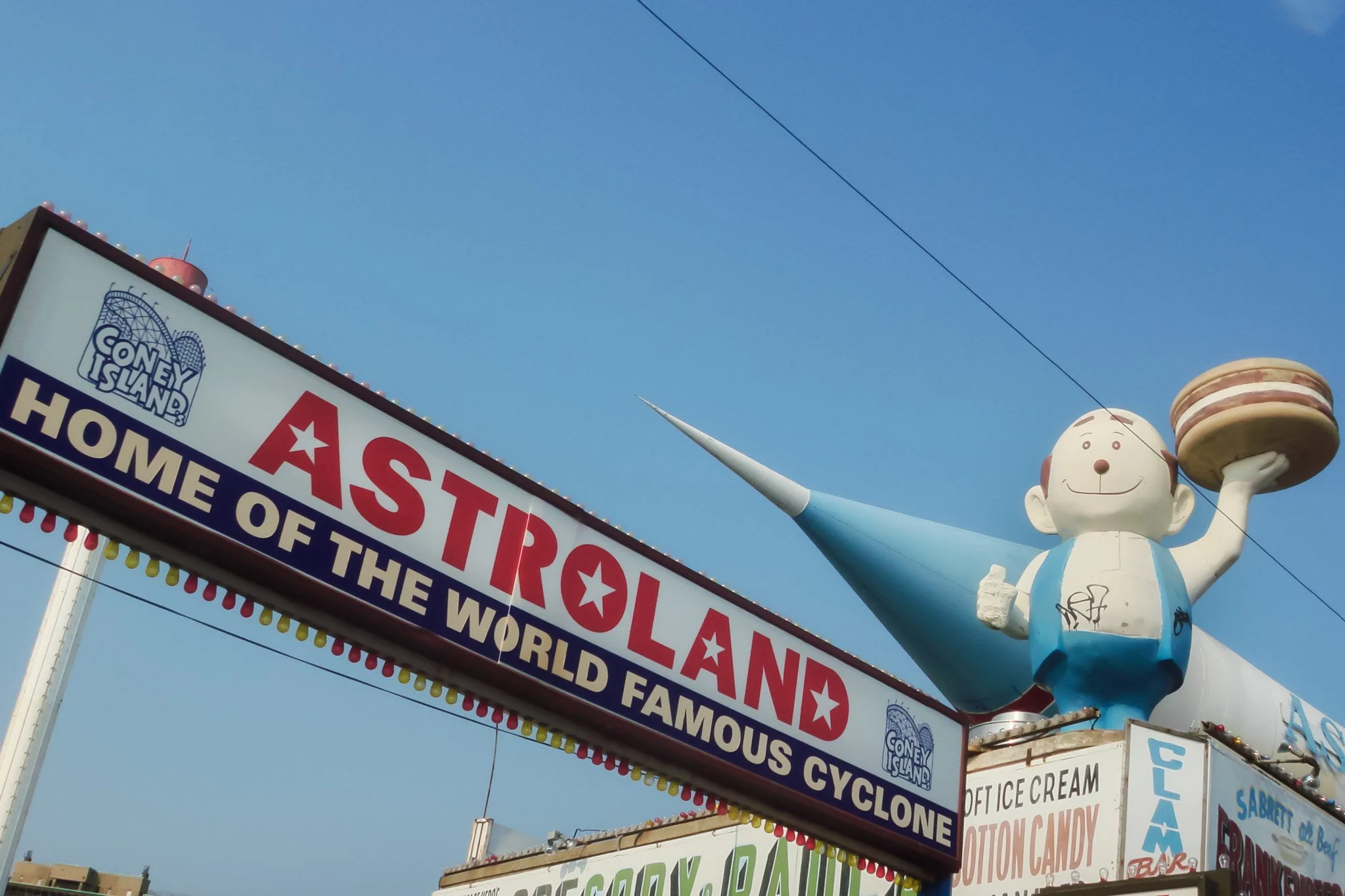 Statue d'un bonhomme tenant une assiette de pancakes, devant un panneau d'attractions de fête foraine Astroland avec un ciel bleu