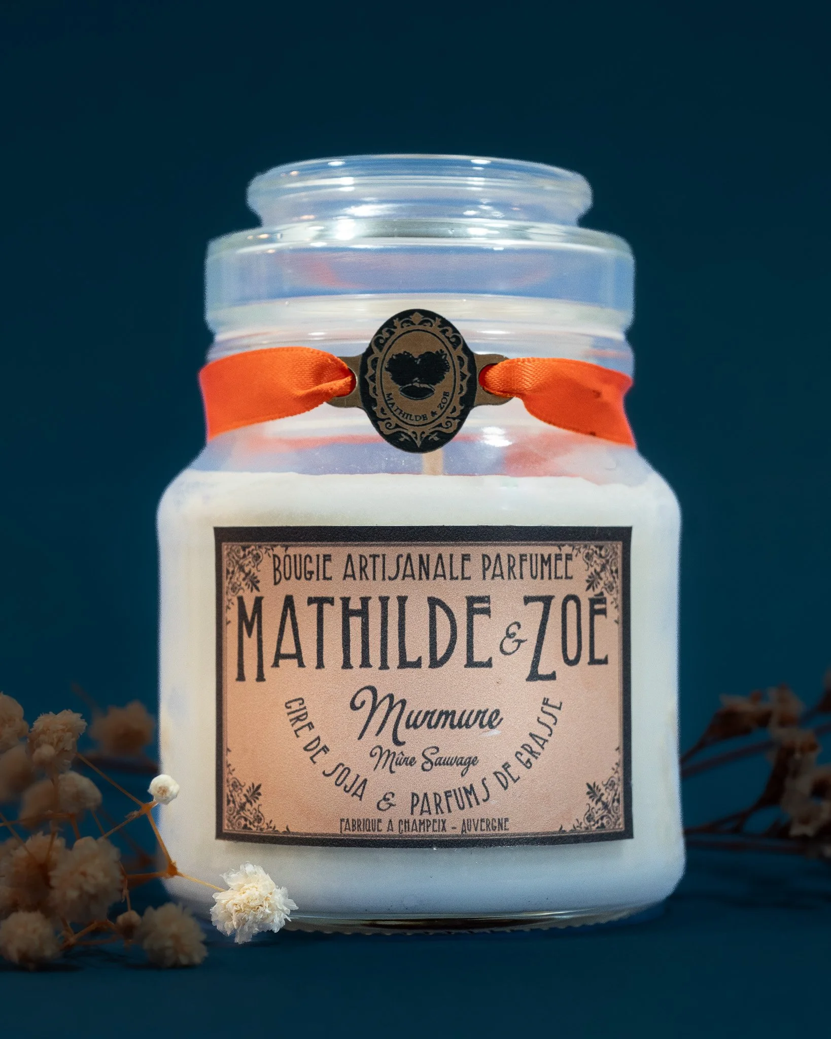 Bougie artisanale en verre parfumée avec un cordon orange , fabriquée en Auvergne, entourée de petites fleurs blanches
