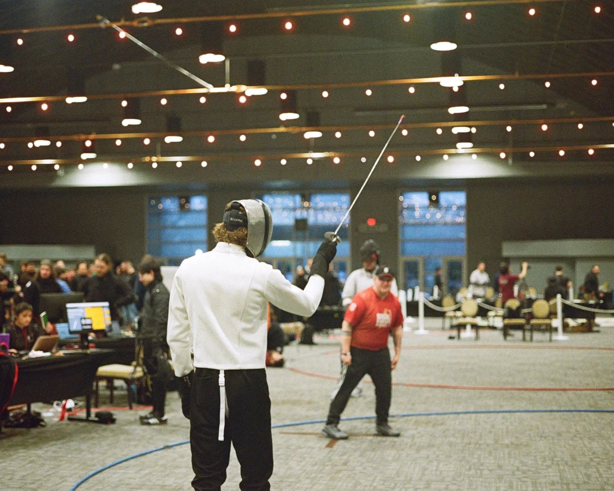 Fencer preparing to engage during America's largest fencing competition, SOCAL SwordFight 2025, populated with spectators and officials.