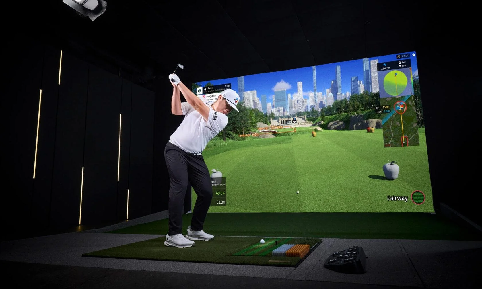 Man in a golf simulator, preparing to hit a golf ball, with a virtual golf course displayed on a large screen in front of him.