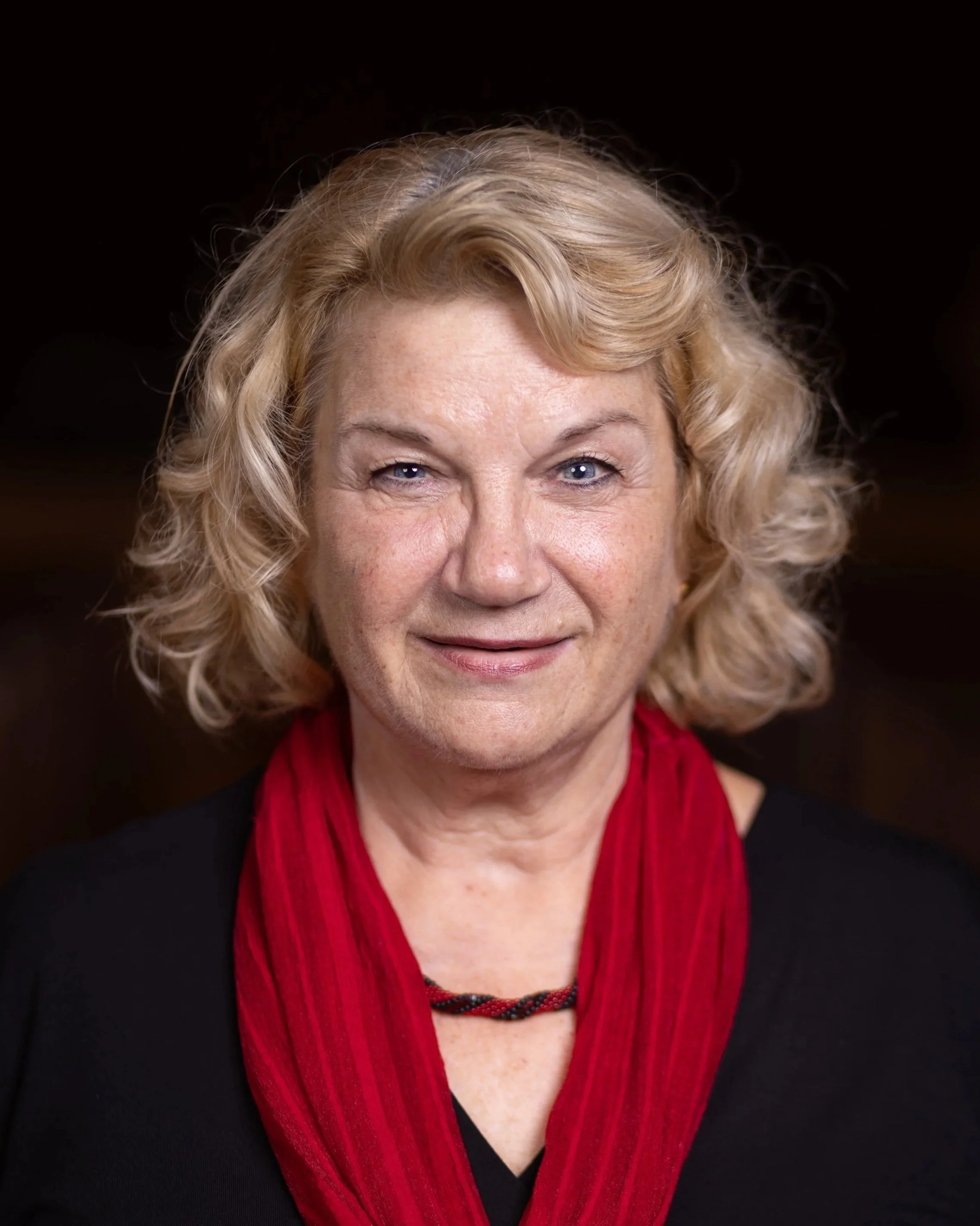Nahaufnahme einer lächelnden Frau mit blonden, lockigen Haaren, das in die Kamera schaut.
