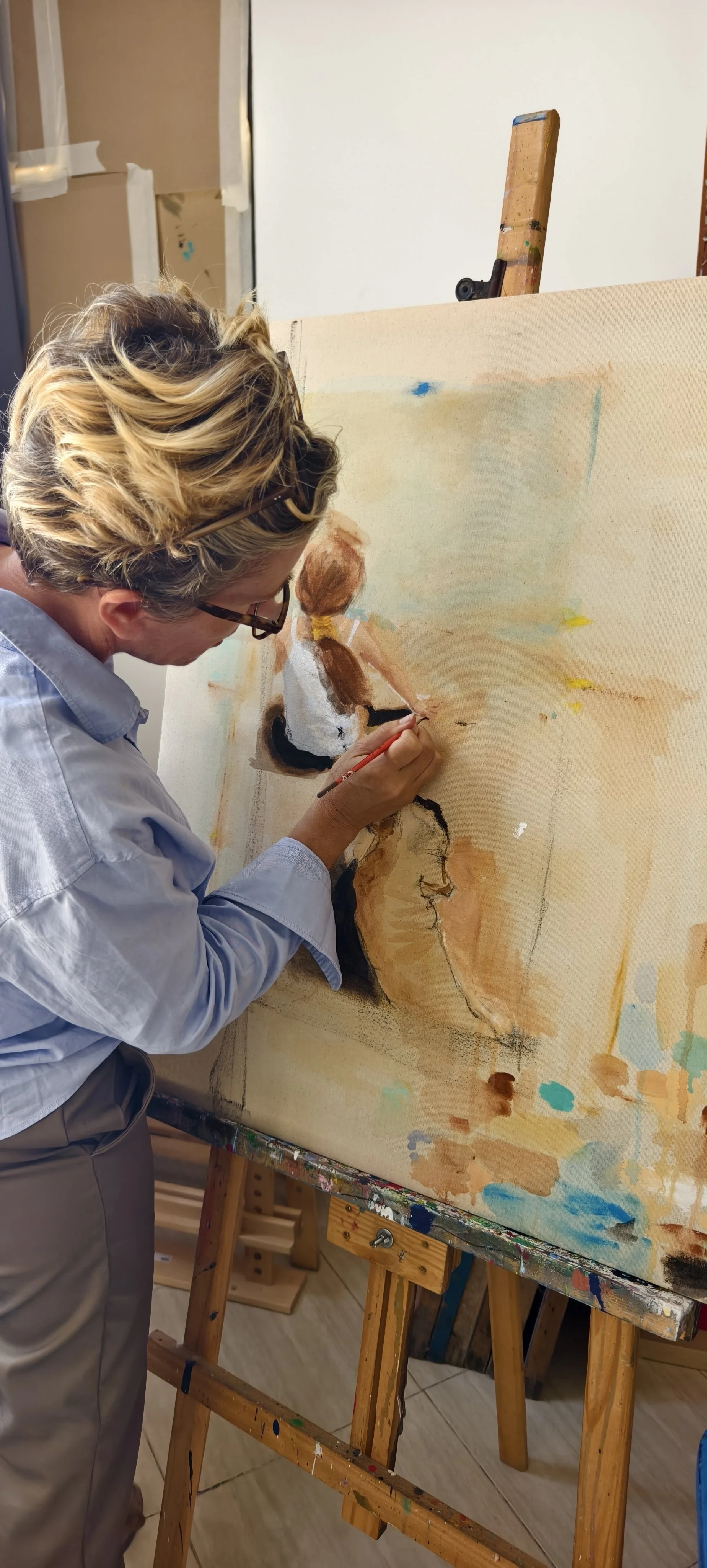 Un artiste peint un tableau d'une femme vue de profil. L'artiste porte des lunettes et une chemise bleue, et travaille sur une toile posée sur un chevalet.