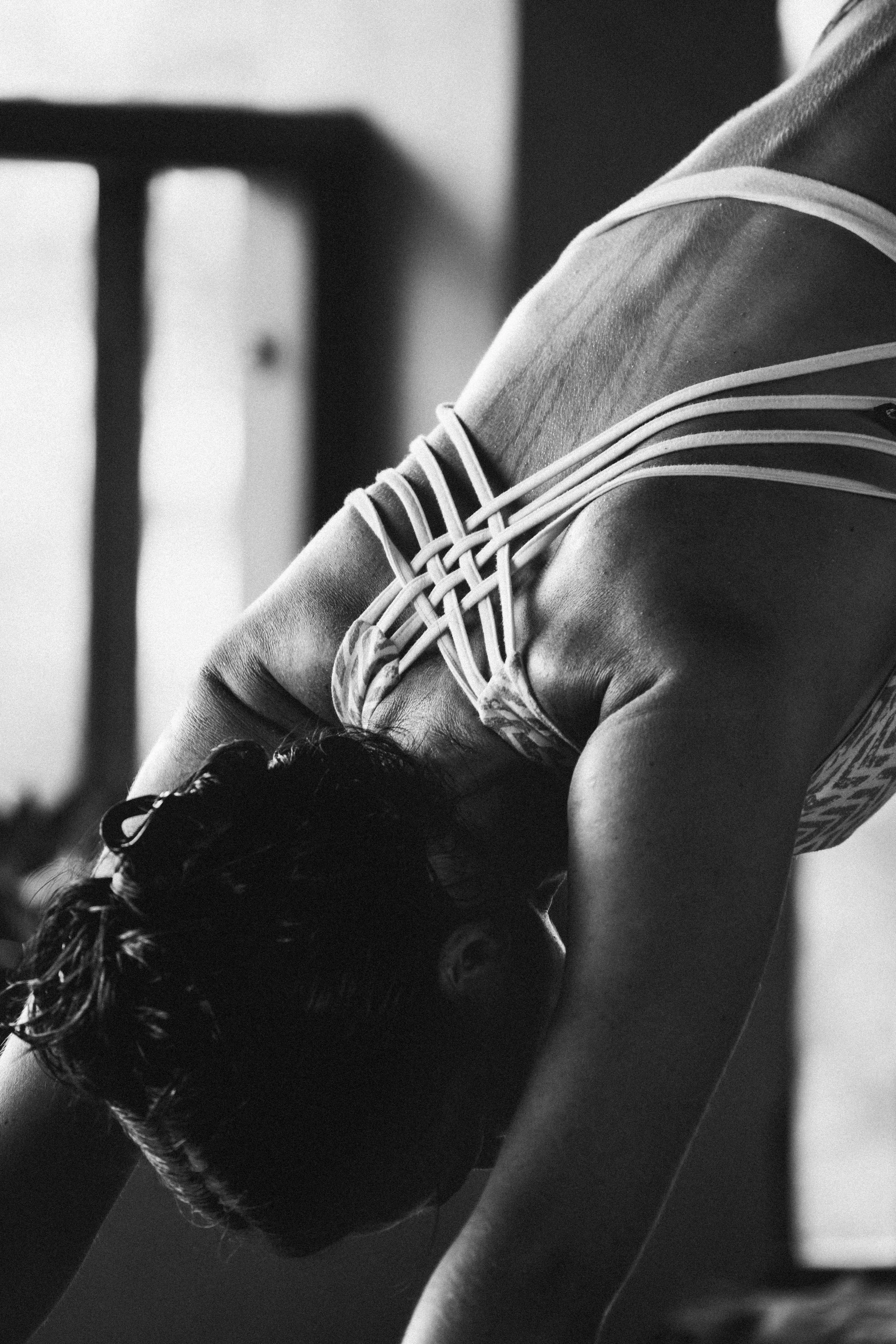 A person with curly hair doing a yoga pose or stretching on a yoga mat in a room, black and white photo.