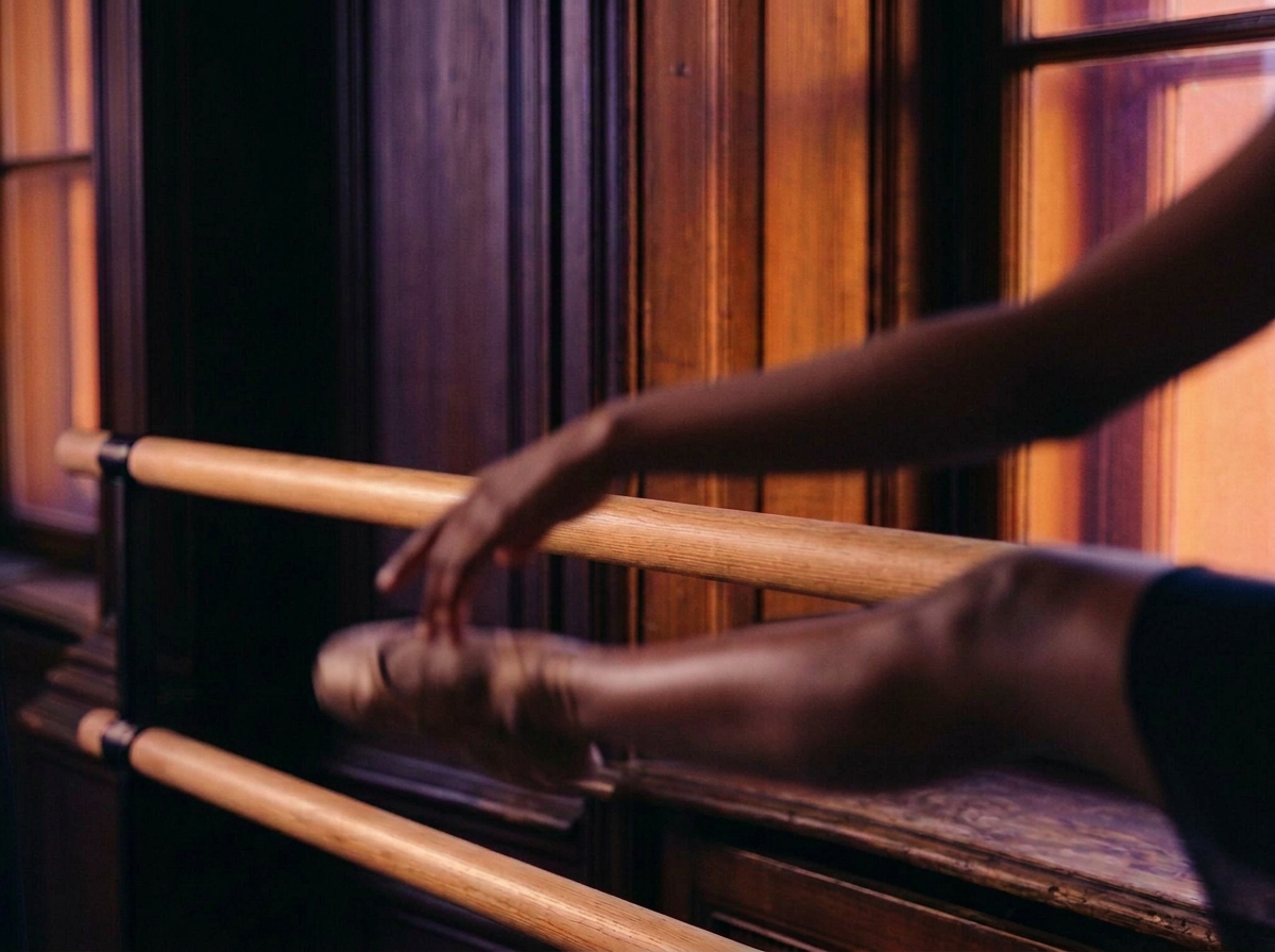 A ballet dancer's legs and feet in pointed ballet shoes stretching on a ballet barre in a dance studio with wooden walls.