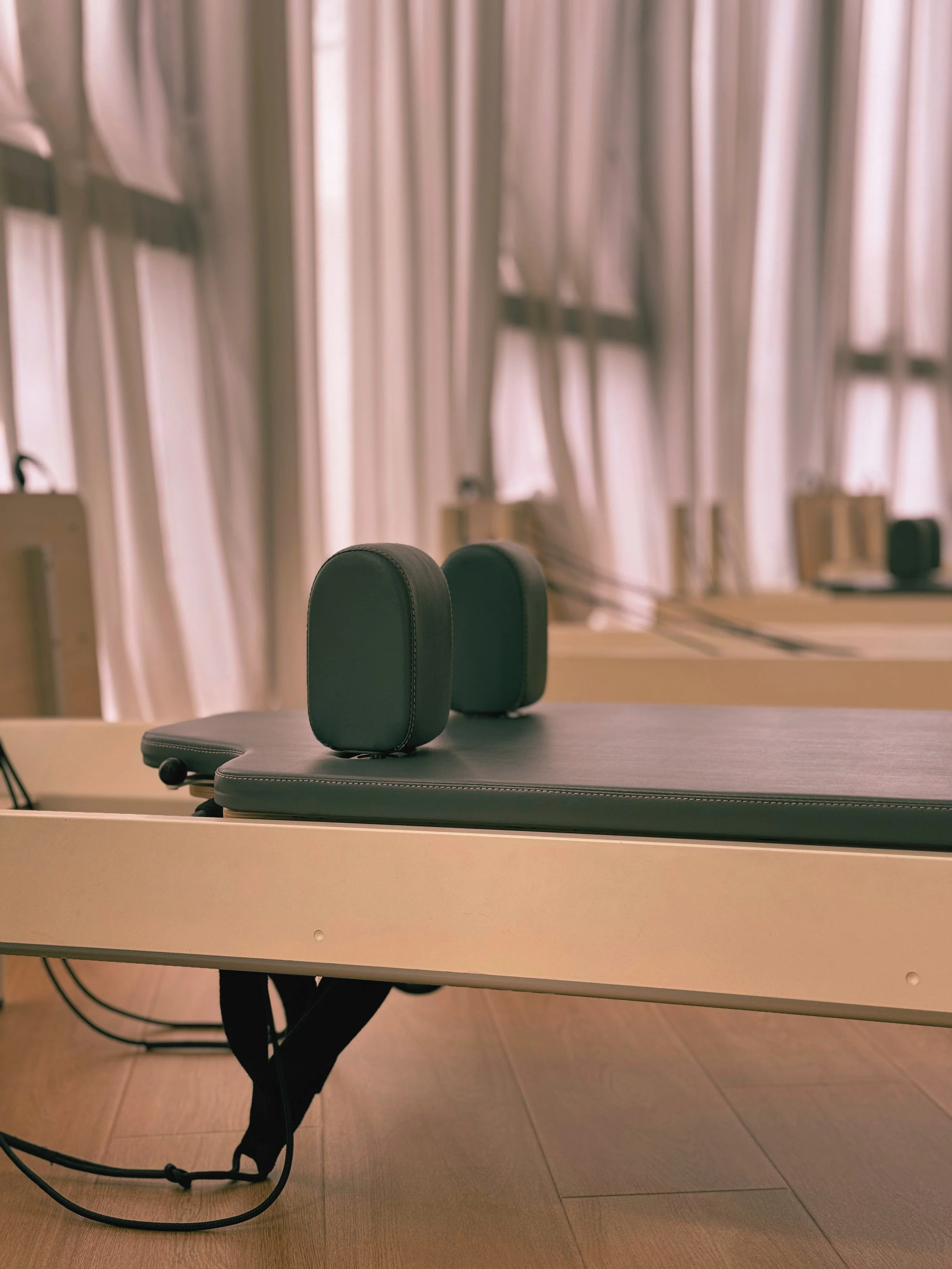 Desk with two black chairs with headrests, behind the desk is a window with beige curtains, and on the desk are some office supplies.