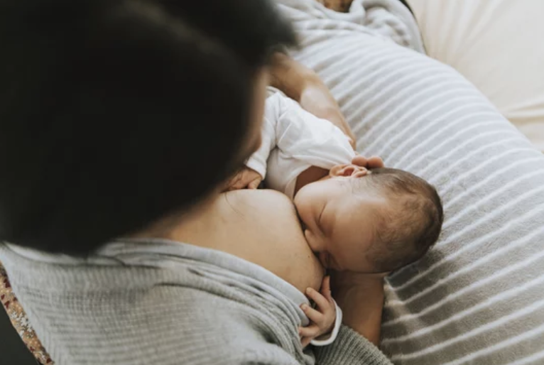 Close-up of a mother breastfeeding her baby while lying on a bed with a striped sheet.