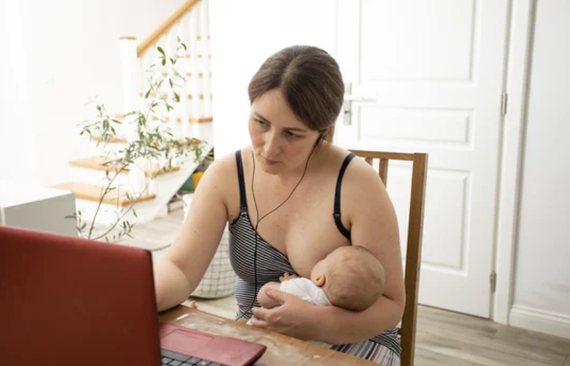 A woman in a striped top breastfeeding a baby while using a laptop.