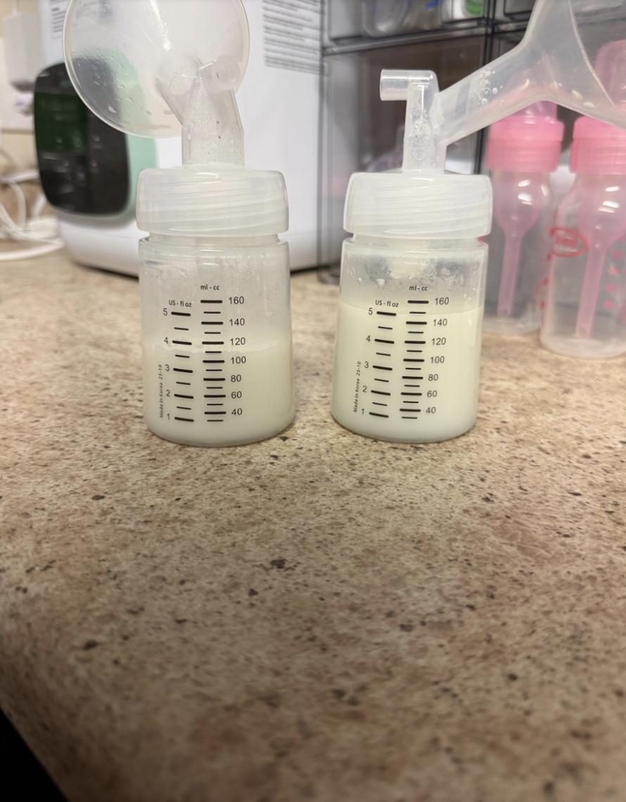 Two small bottles filled with breast milk on a kitchen counter, with breast pump parts attached to each bottle.