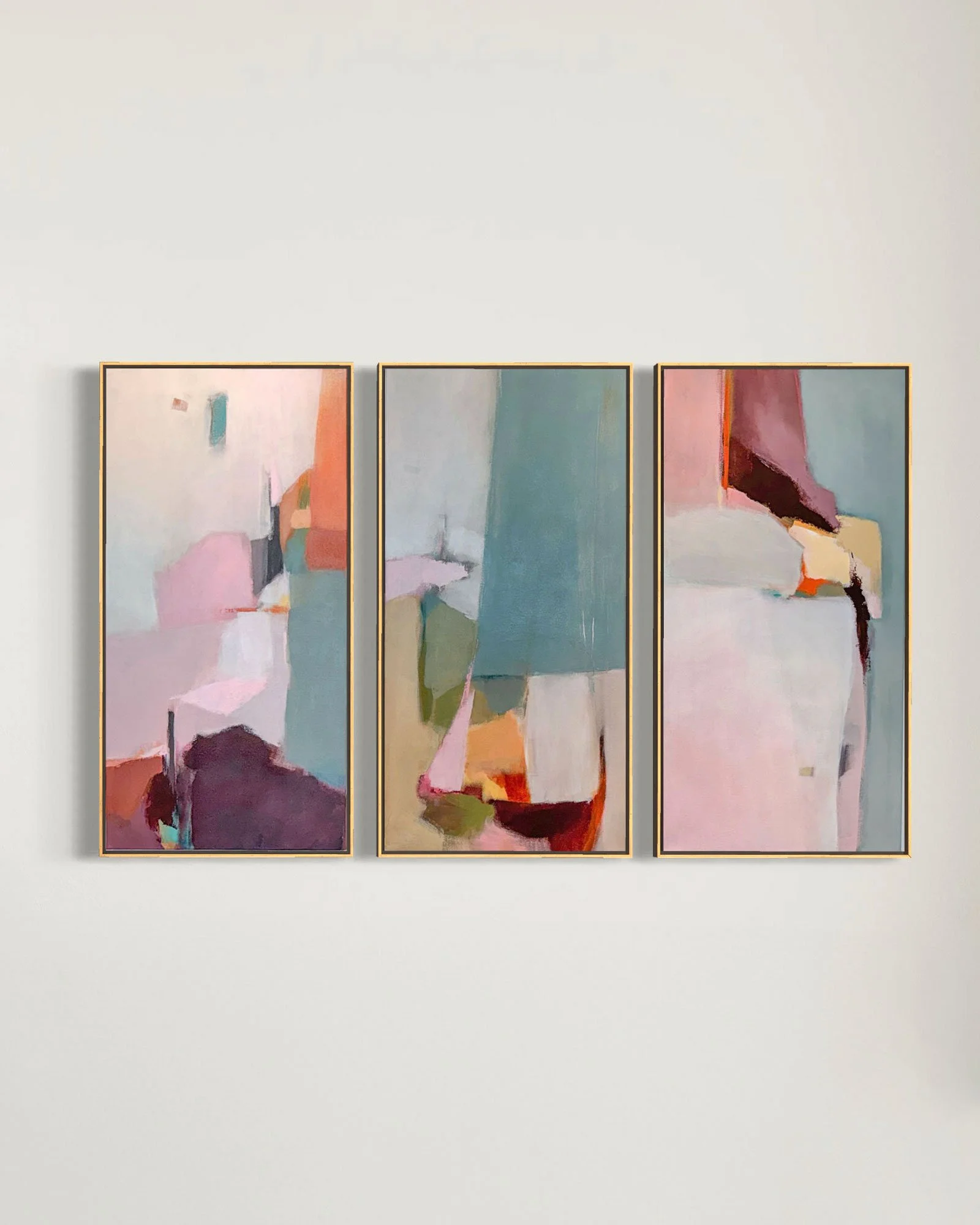 Three abstract paintings with pastel colors and geometric shapes are hanging side by side on a plain white wall.
