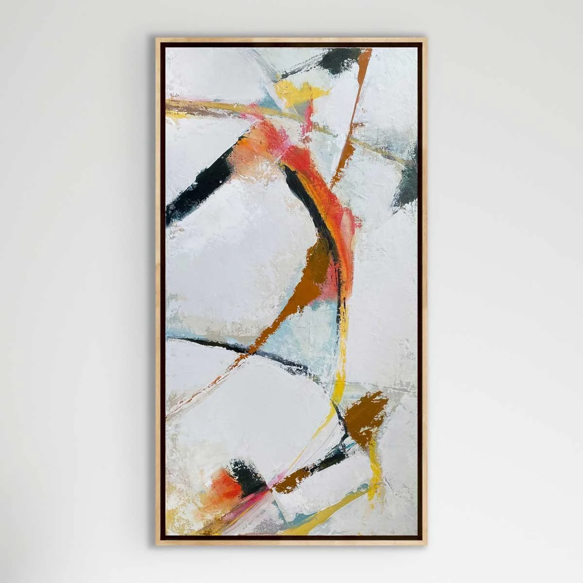 Abstract painting with bold splashes of black, red, orange, yellow, and light blue on a white background, framed in light wood.