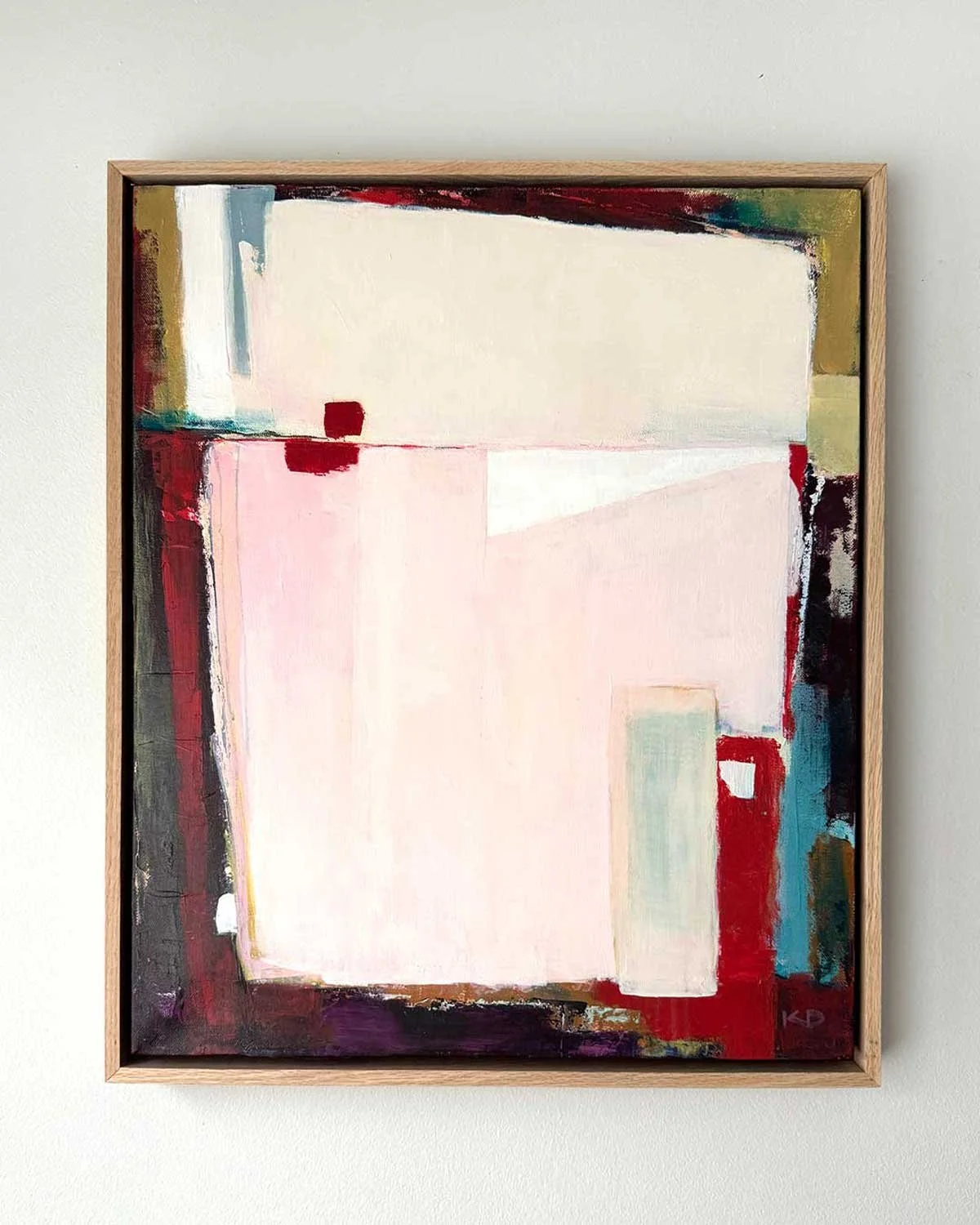 Abstract painting with large pink and white shapes, red, black, green, blue, and beige accents on canvas framed in light wood.