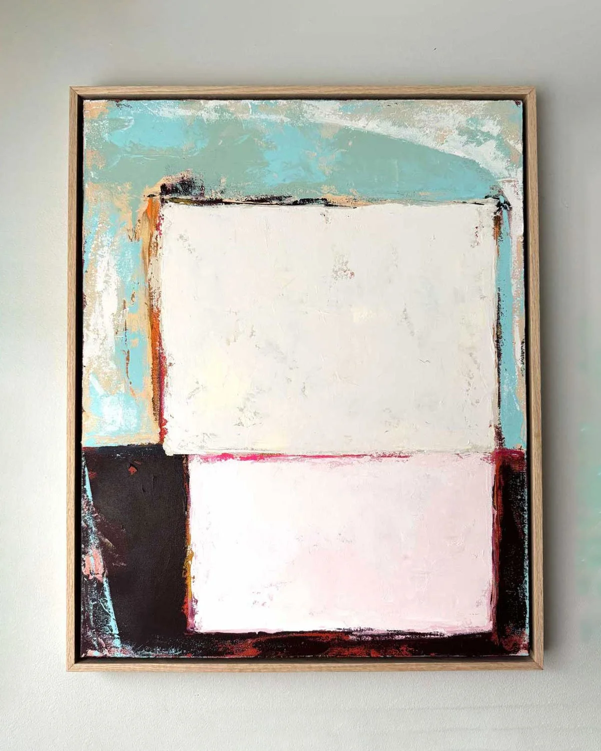 Abstract painting with blocks of color, including white, black, red, and shades of blue, framed and hung on a light-colored wall.