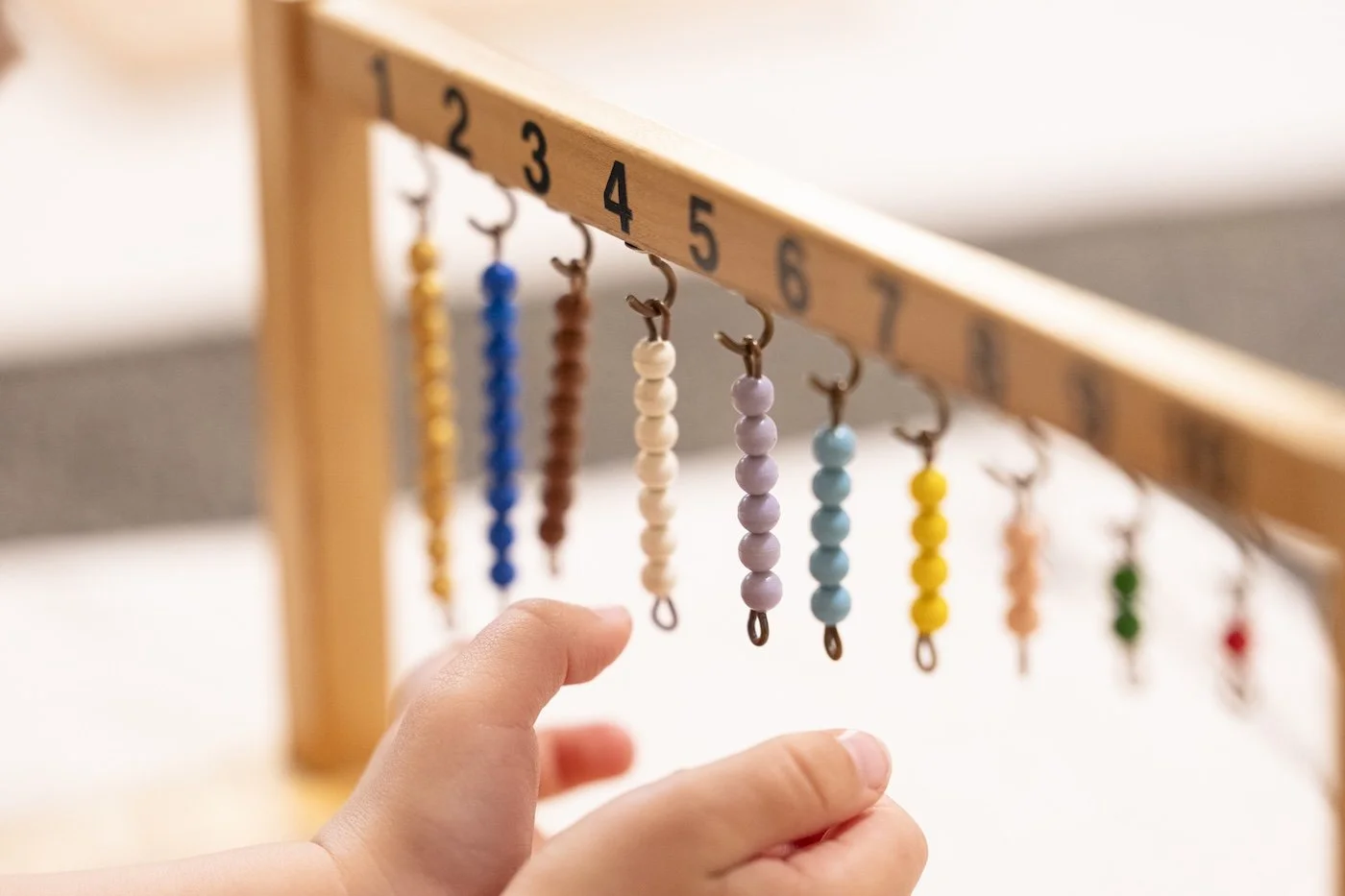 A person's hand reaching for beaded earrings hanging from a numbered wooden rack, with earrings in various colors.
