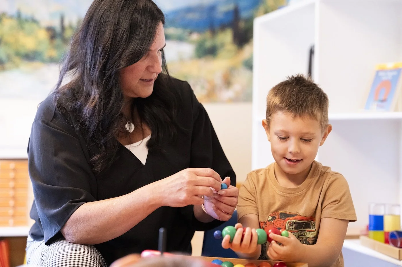 A woman and a young boy playing with colorful toy balls at a table in a bright room.