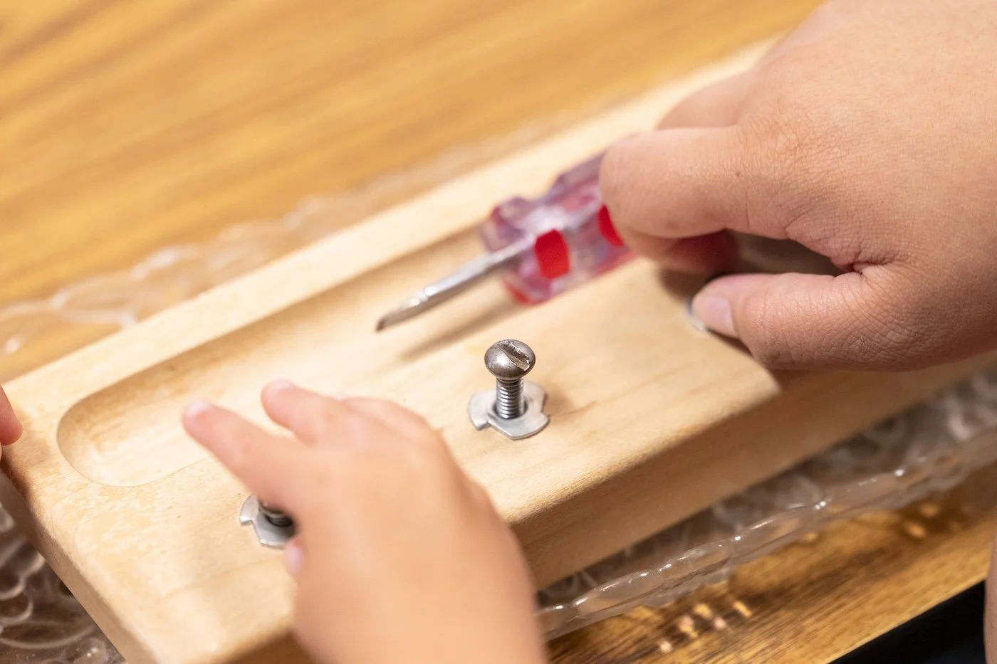 A person using a screwdriver to tighten a screw on a wooden piece with metal washers.