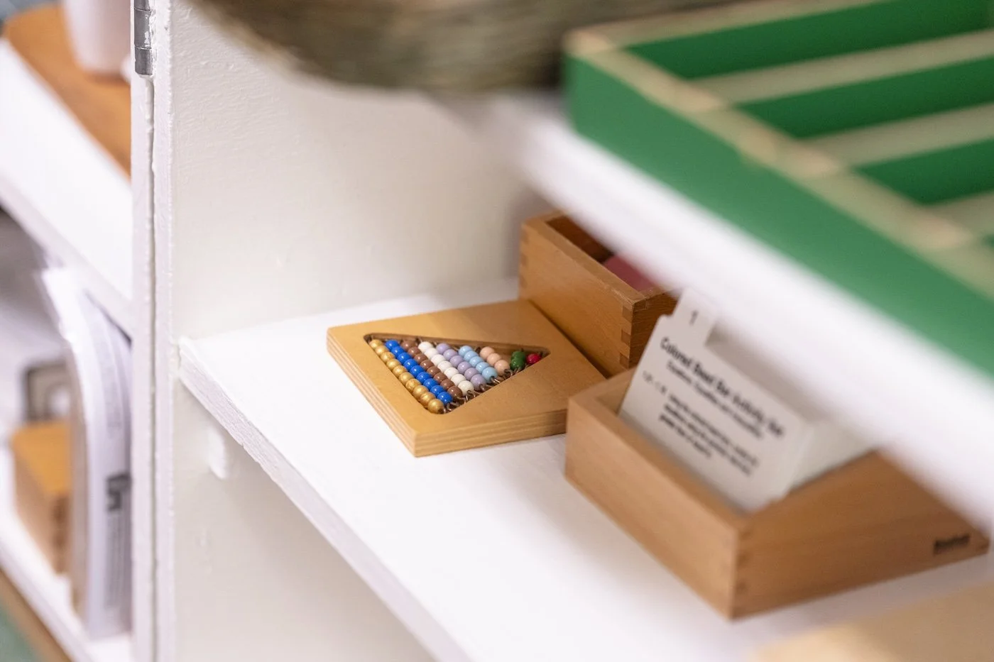 A wooden box containing colorful small beads on a white shelf.