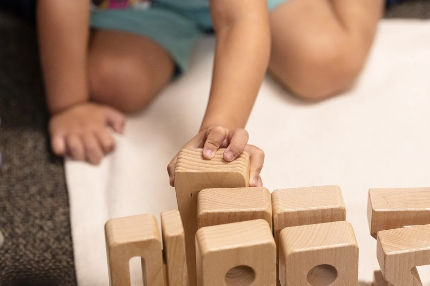 A child kneeling on the floor stacking wooden blocks.