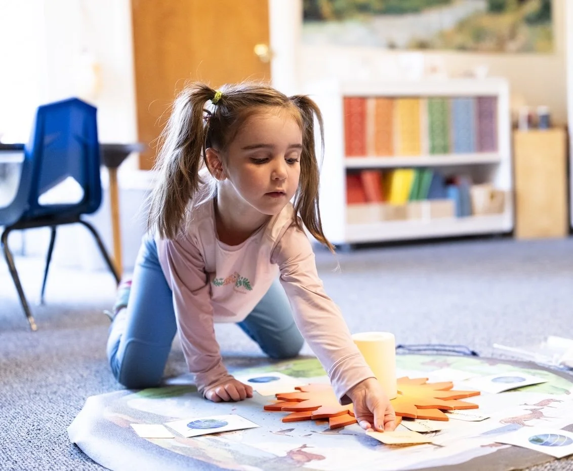 A young girl is playing on the floor with various colorful foam cutouts and pictures in a classroom setting.