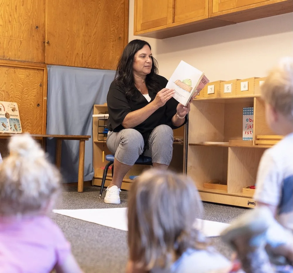A woman reading a children's book to a group of young kids in a classroom setting.