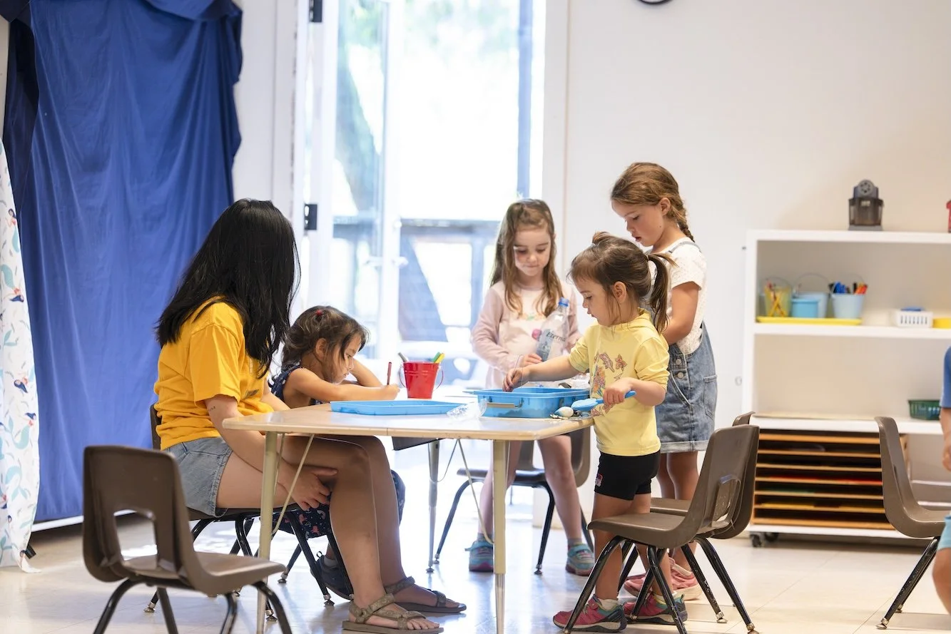 Group of young children engaging in arts and crafts activity at a table in a classroom.