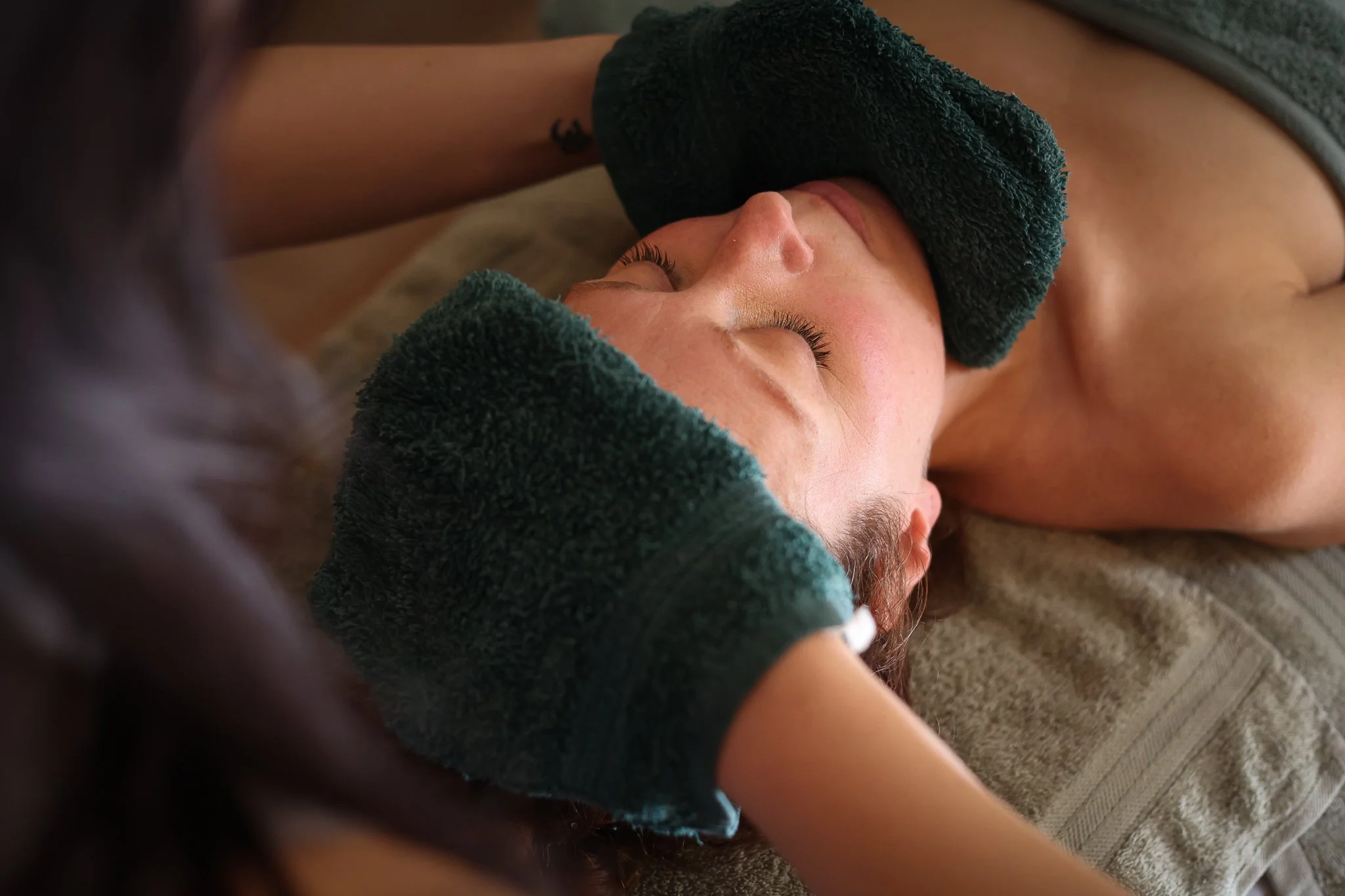 A person lying on a bed have a hot towel face steam as part of an anti ageing Organic facial.
