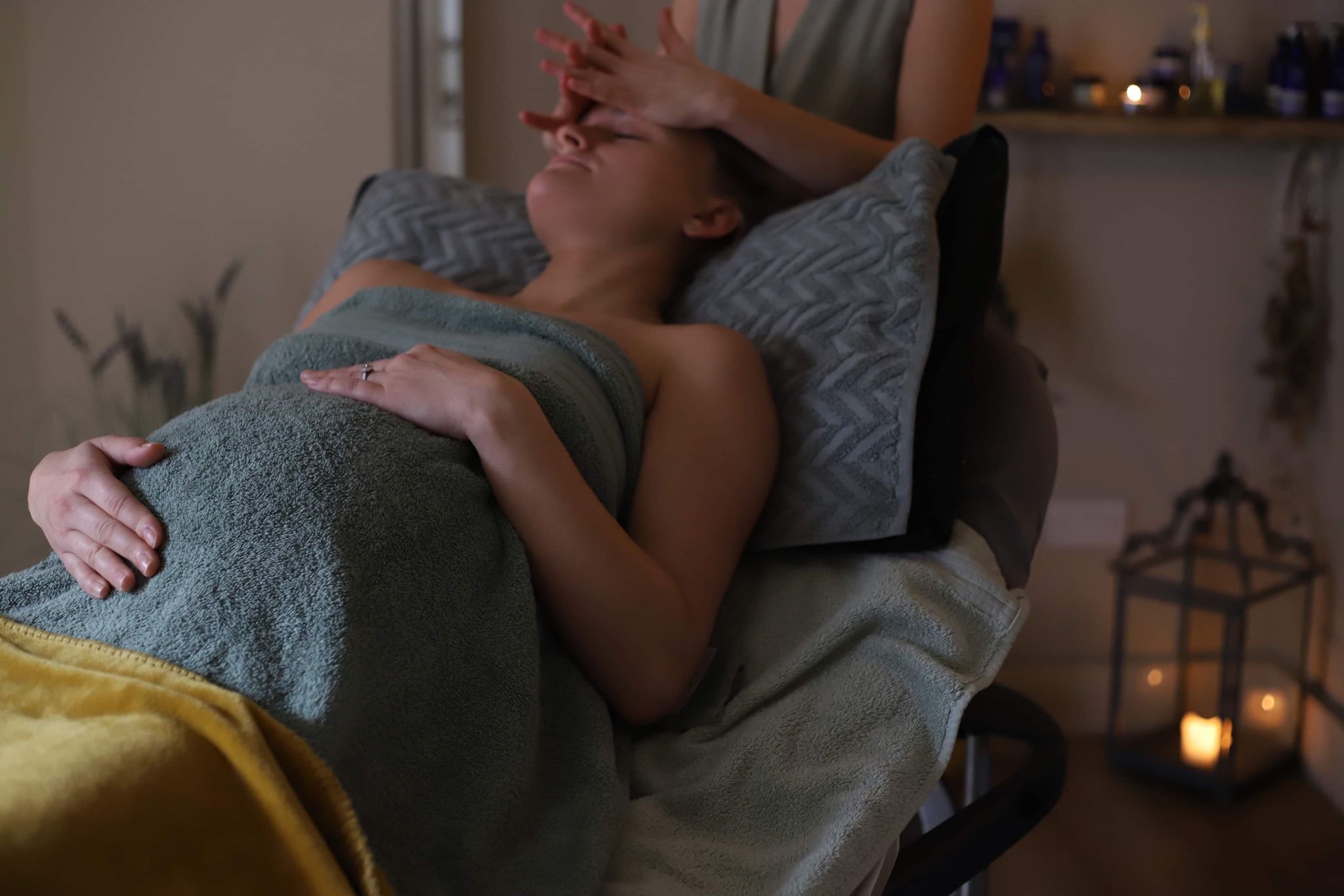 A pregnant lady lies propped up on a bed recieving a Re-hydrating Neal's Yard Remedies facial and nurturing pregnancy massage.