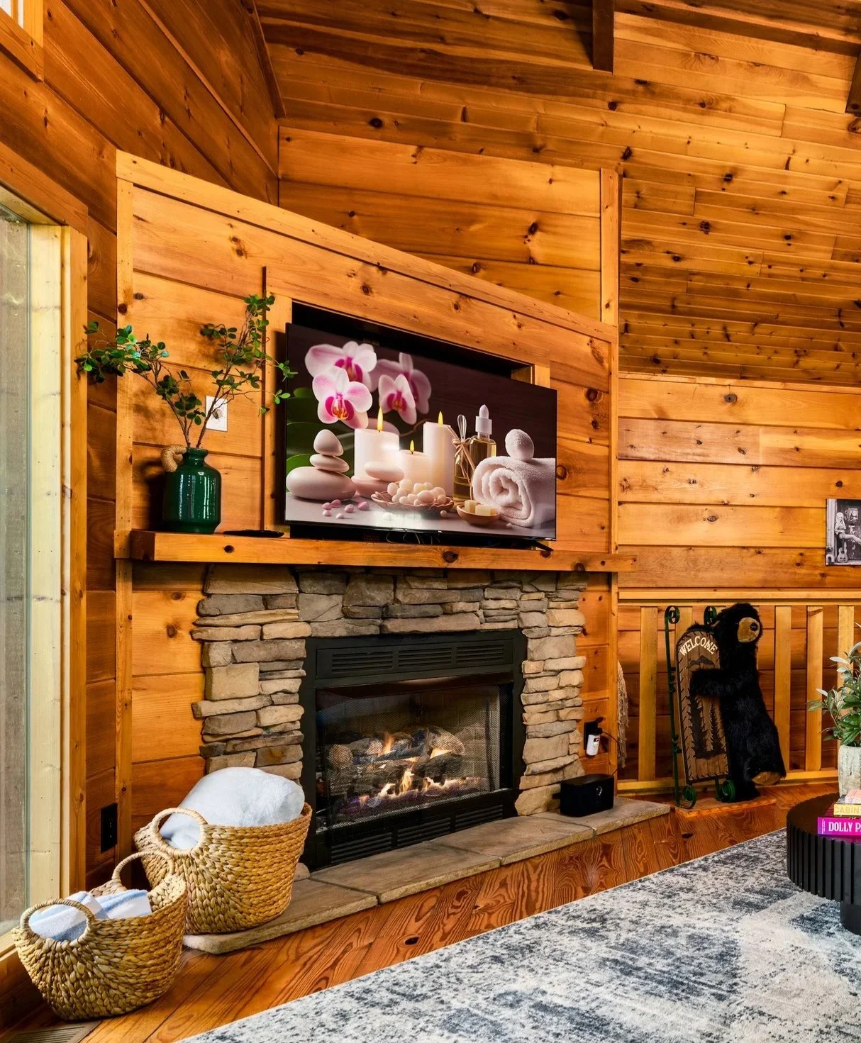 Blue Sage Hideaway's cozy living room with wooden walls and chimney featuring a flat-screen TV displaying a spa scene with candles, orchids, and stones.
