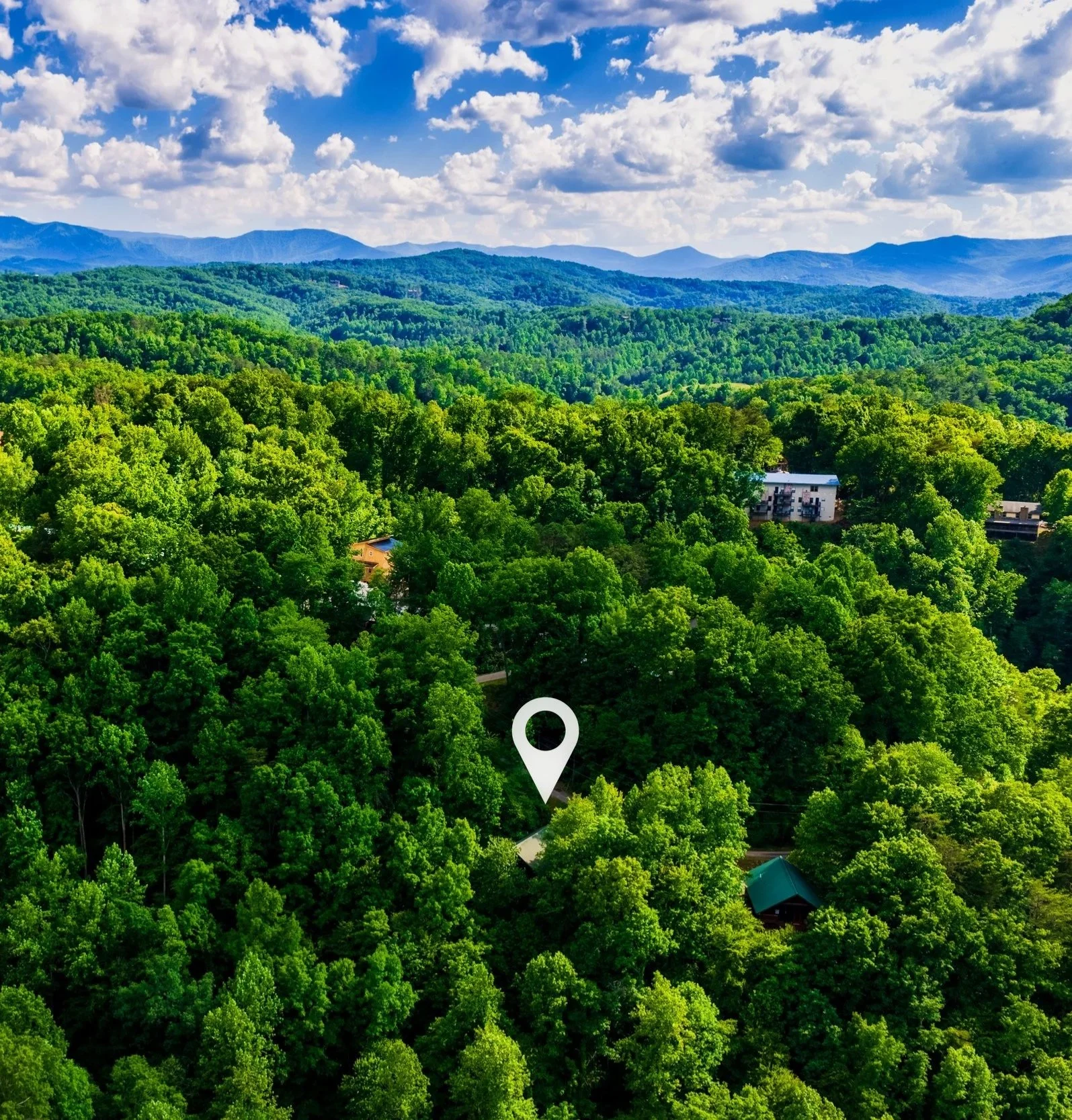 Aerial view of dense green forest with a few buildings, mountains in the background, and a partly cloudy sky pointing to Blue Sage Hideaway