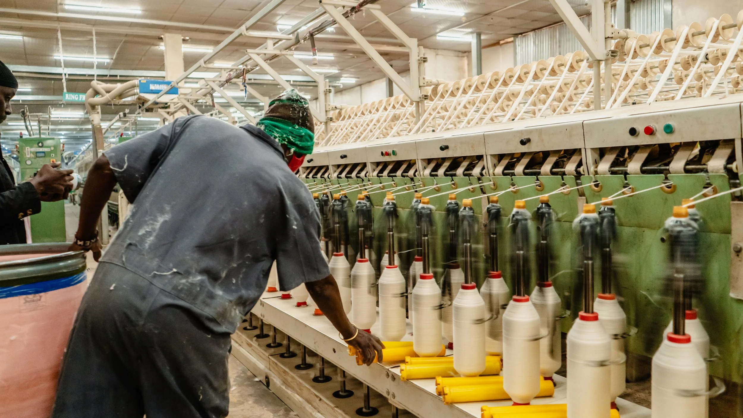 Workers operate textile machinery in a factory setting, spinning yarn onto large cones.