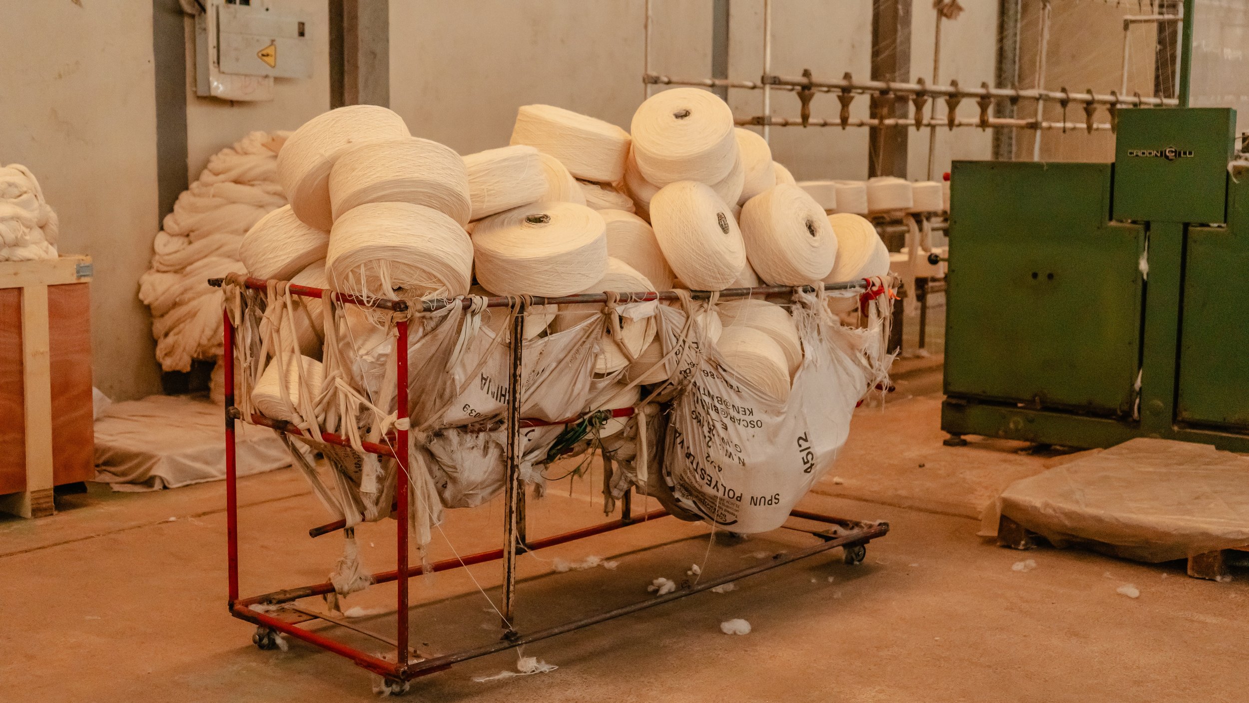 A large metal cart filled with large spools of white yarn, situated in an industrial or factory setting.