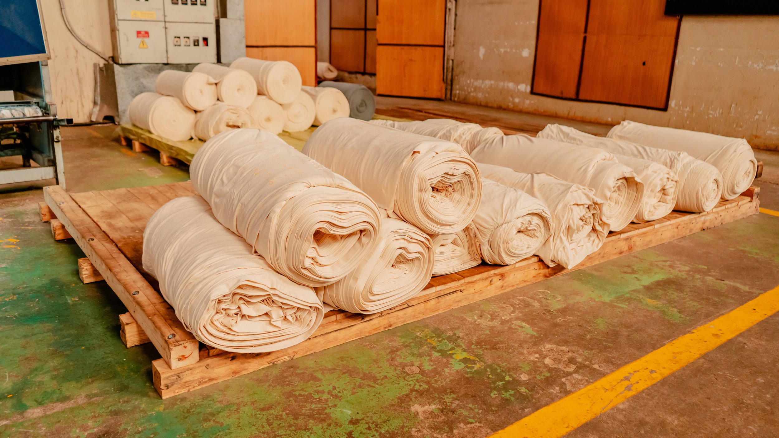 Large rolls of fabric stacked on a wooden platform in an industrial workspace.
