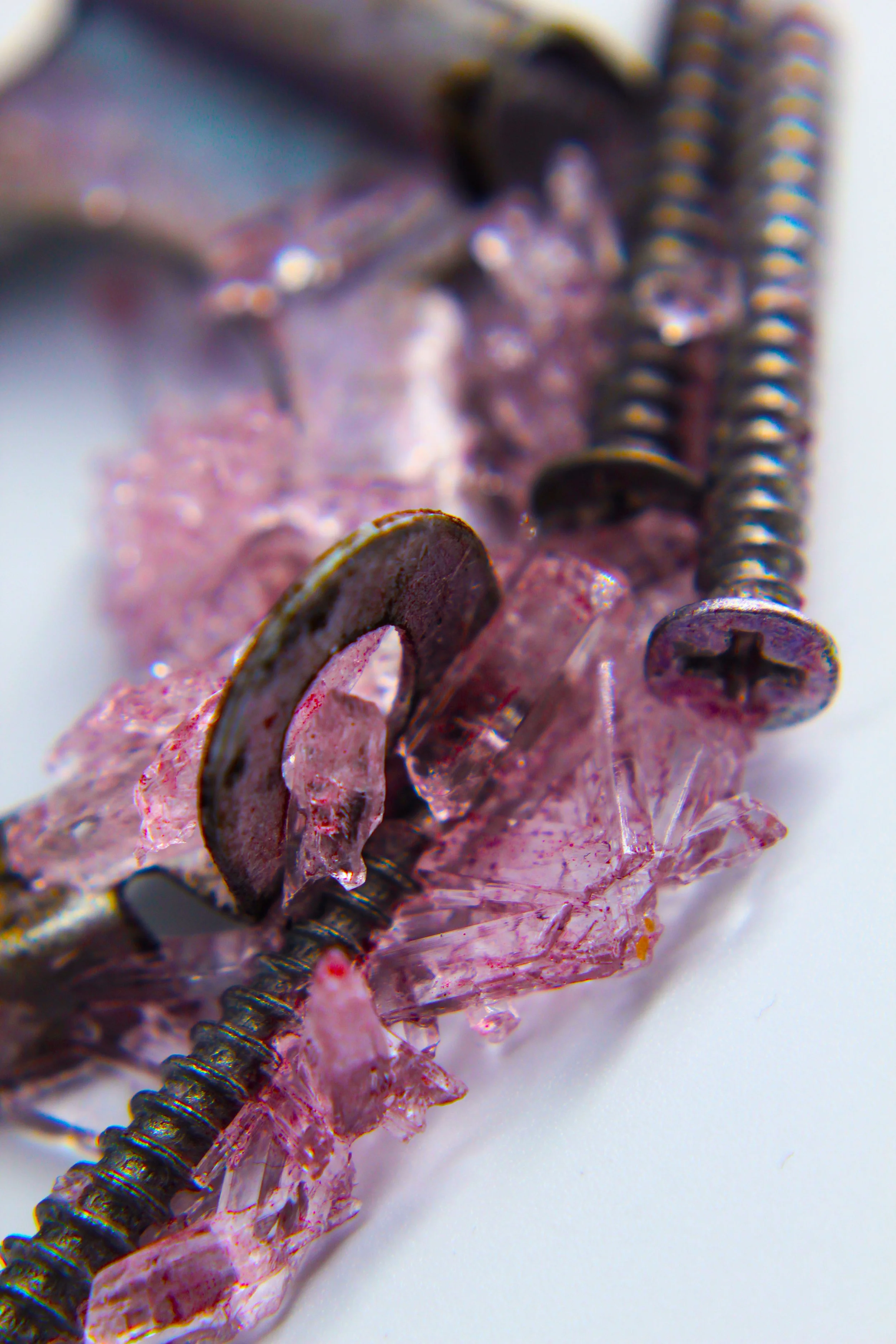 Close-up view of a screw, a lot of pinkish rock fragments, and some thin, black, coiled wires or springs.