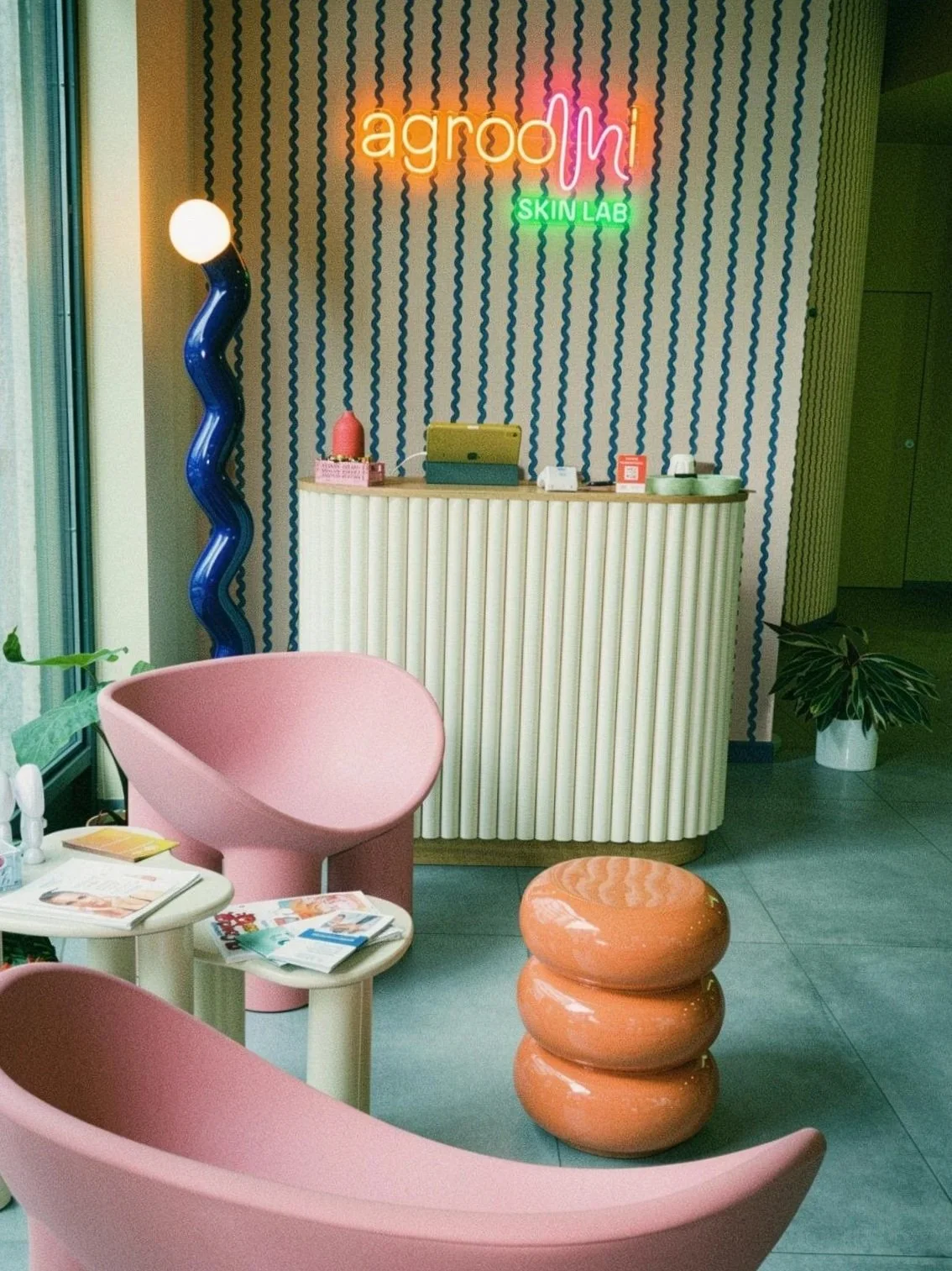Interni di un centro estetico o spa con arredi moderni e colorati, tra cui sedie rosa e un'illuminazione a neon con la scritta 'agrodi SKIN LAB'.