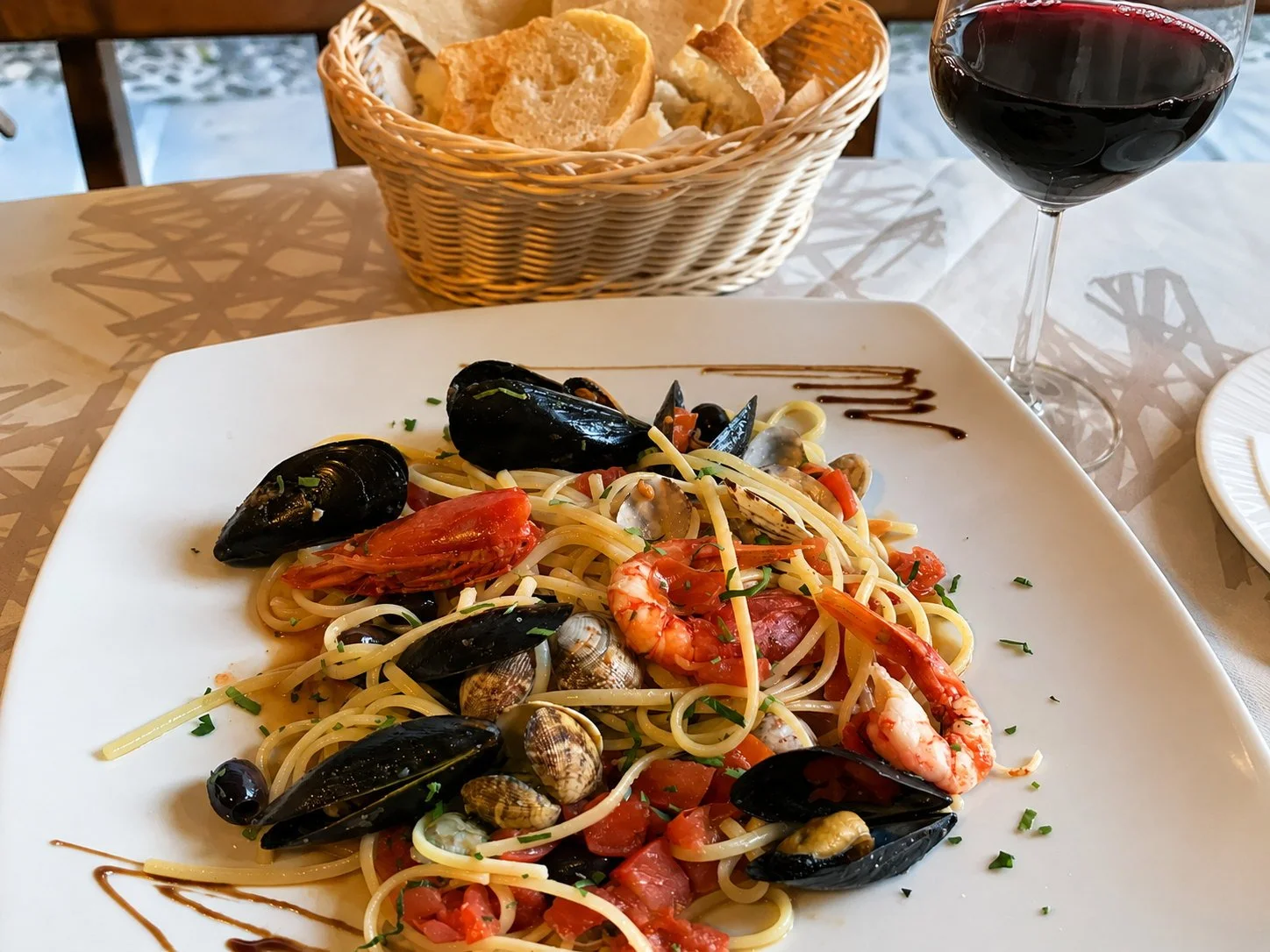 Seafood pasta with mussels, clams and prawns beside a glass of red wine
