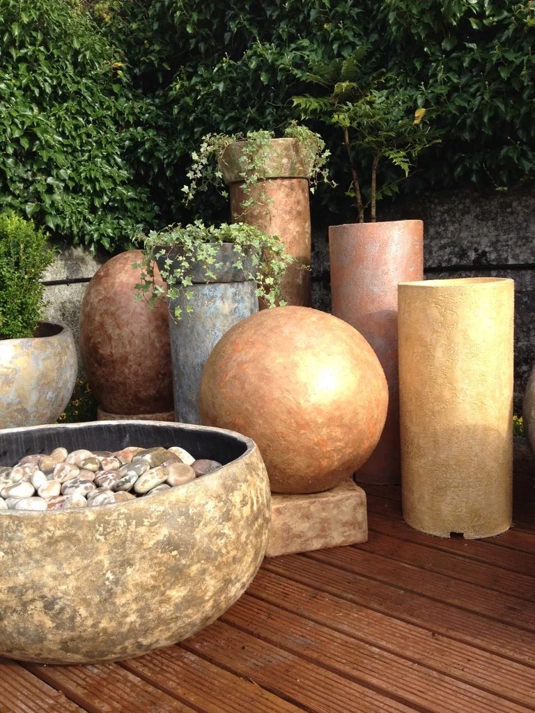 Various large patio planters and pots with plants and stones on a wooden deck.