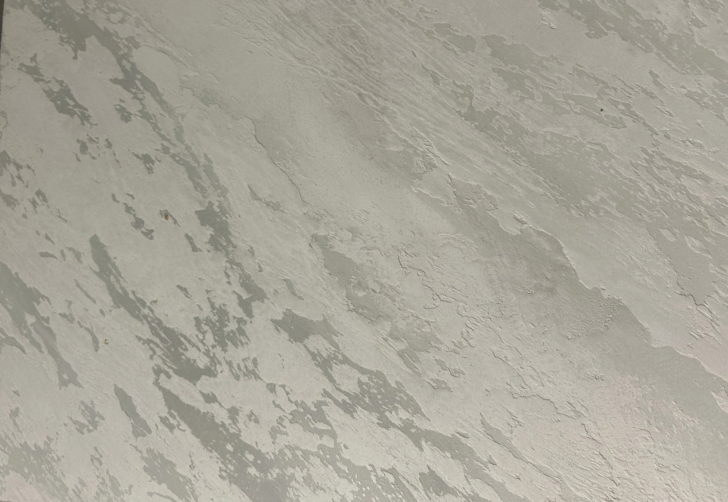 Close-up of a textured, painted ceiling with cracks and peeling paint.