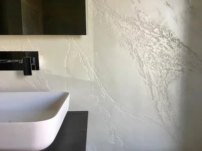 Bathroom with a rectangular mirror, white vessel sink, and a black faucet, with textured off-white wall.