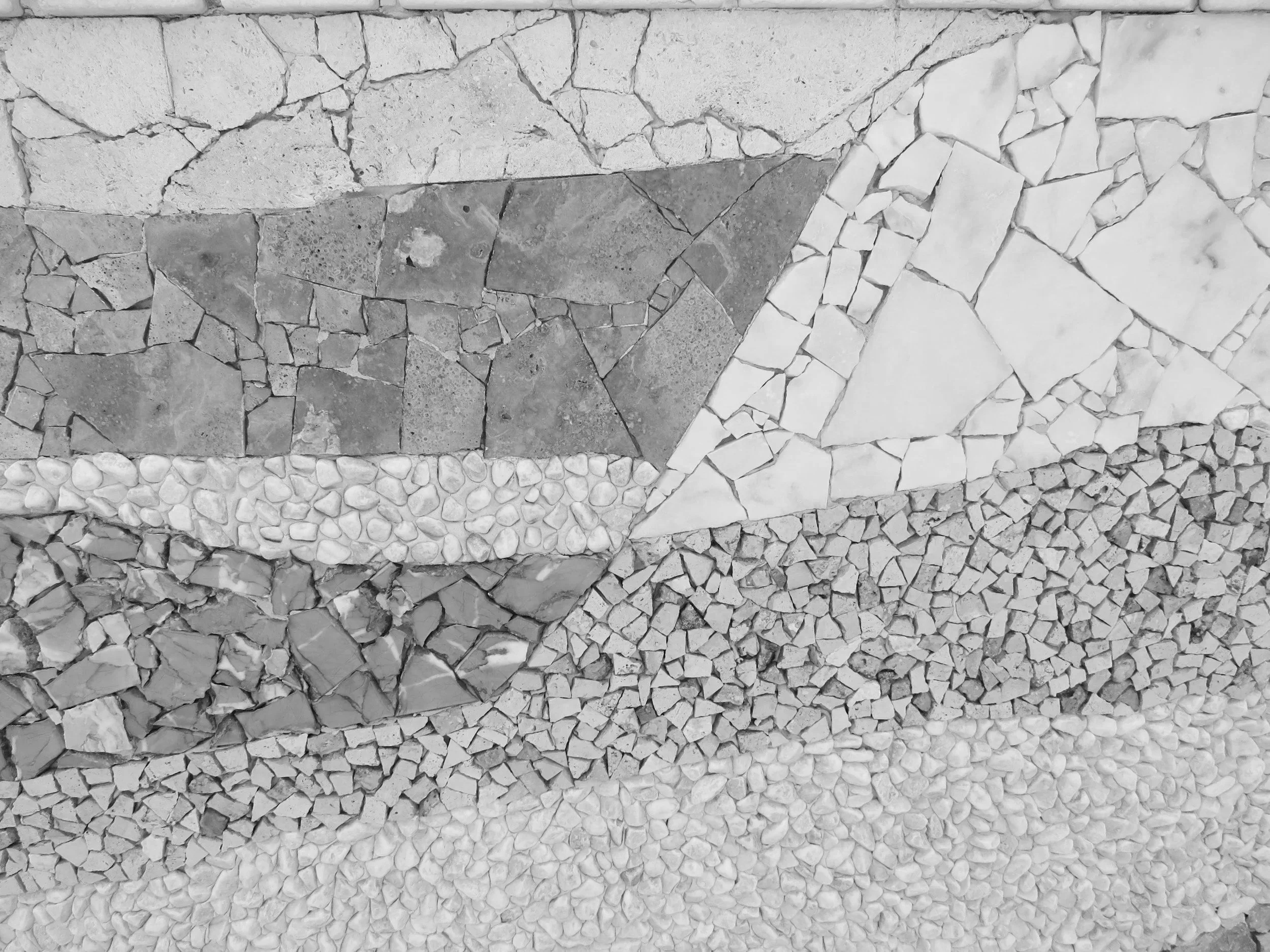 Array of stone mosaic tiles in various shapes and sizes, arranged in geometric patterns, in shades of gray and white.