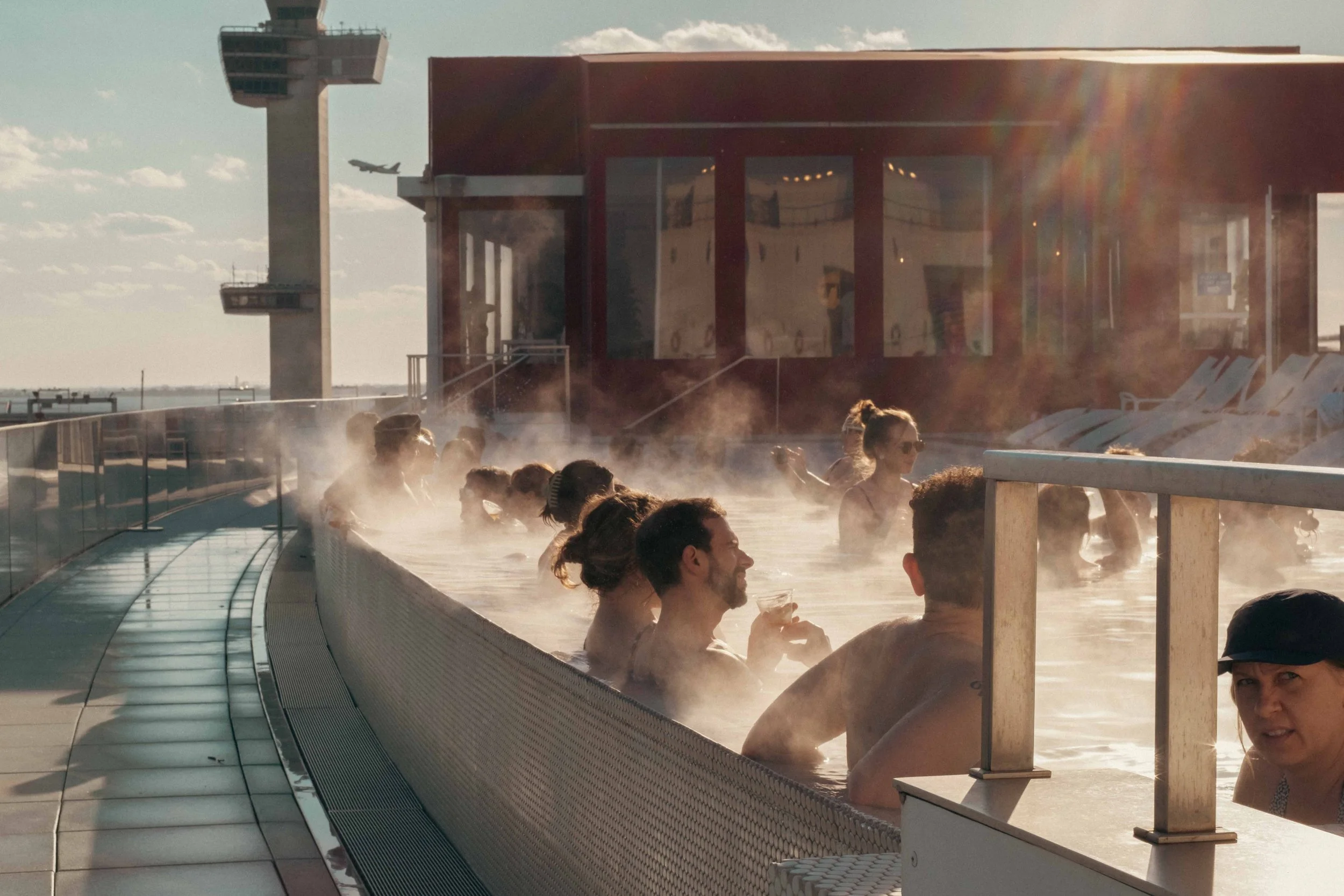 People enjoying hot spring bath on a rooftop with city and airplane view in the background.