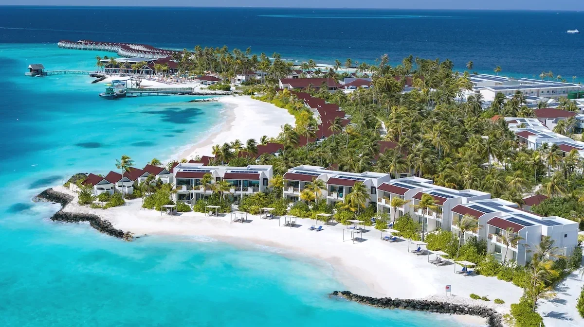 Aerial view of OBLU XPERIENCE Ailafushi, with beachfront accommodation, white sand, palm trees and a turquoise Maldivian lagoon.