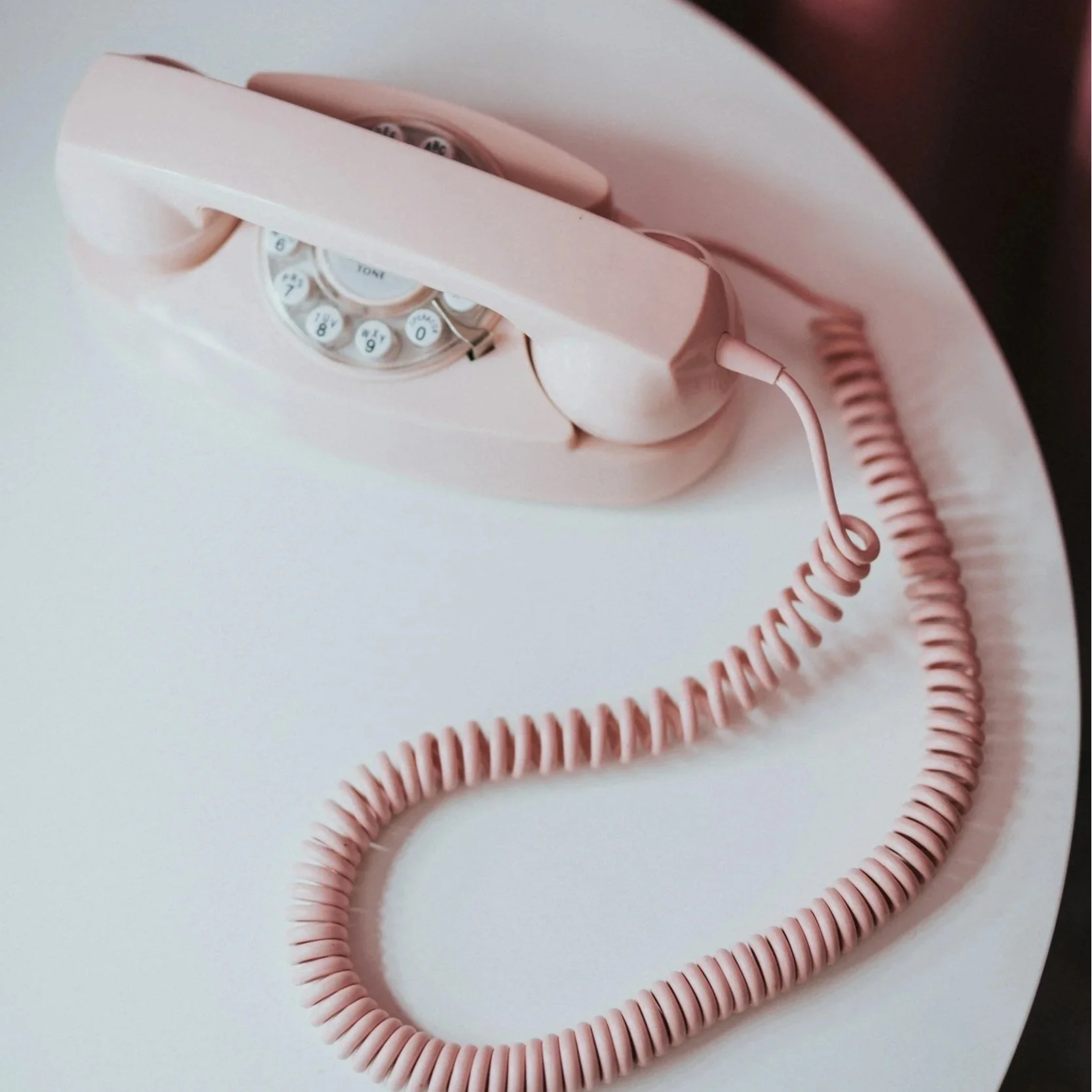 Close-up of a vintage pink rotary telephone with a coiled cord on a white surface.
